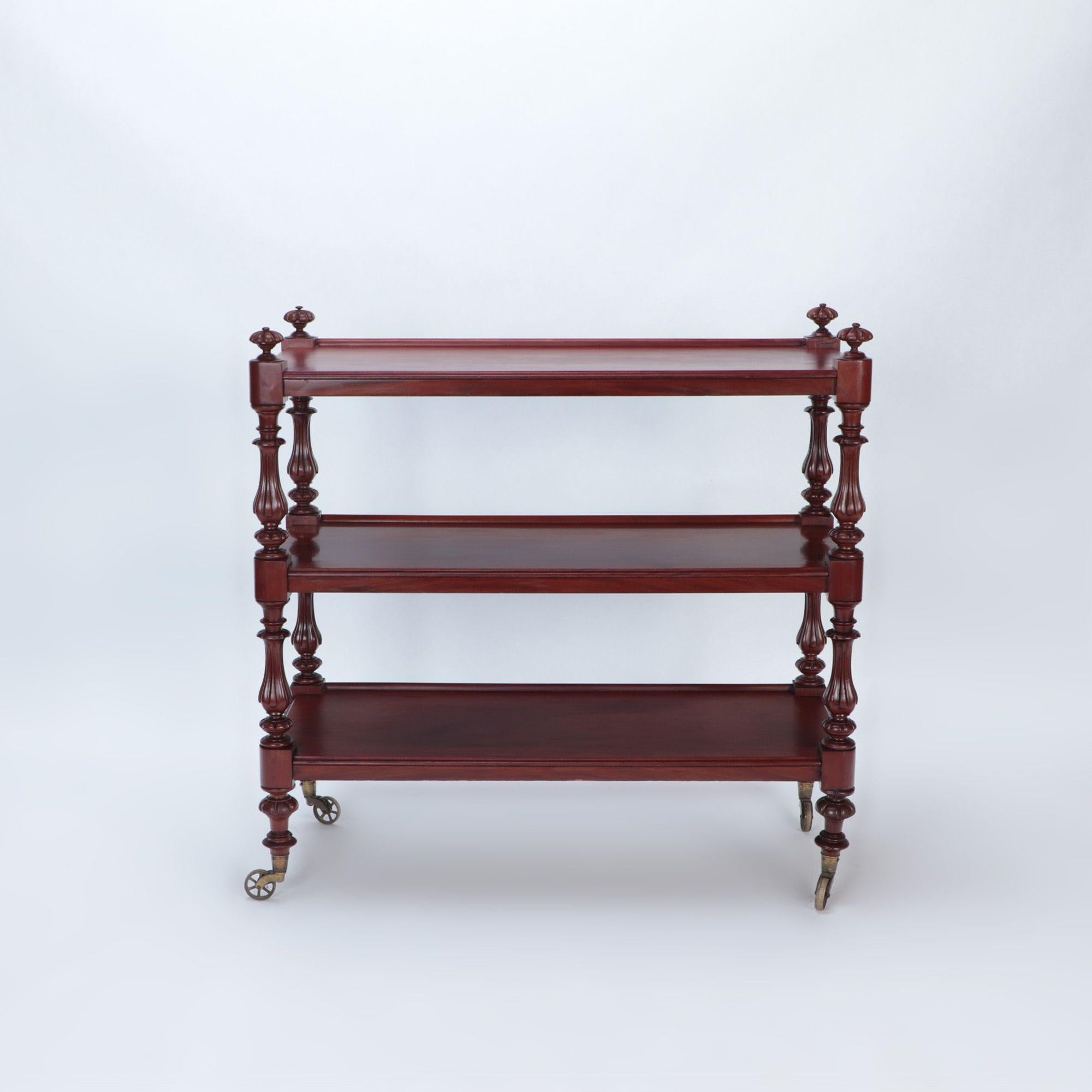 An English mahogany 19th century three tier dessert on wheels having shaped and carved columns.