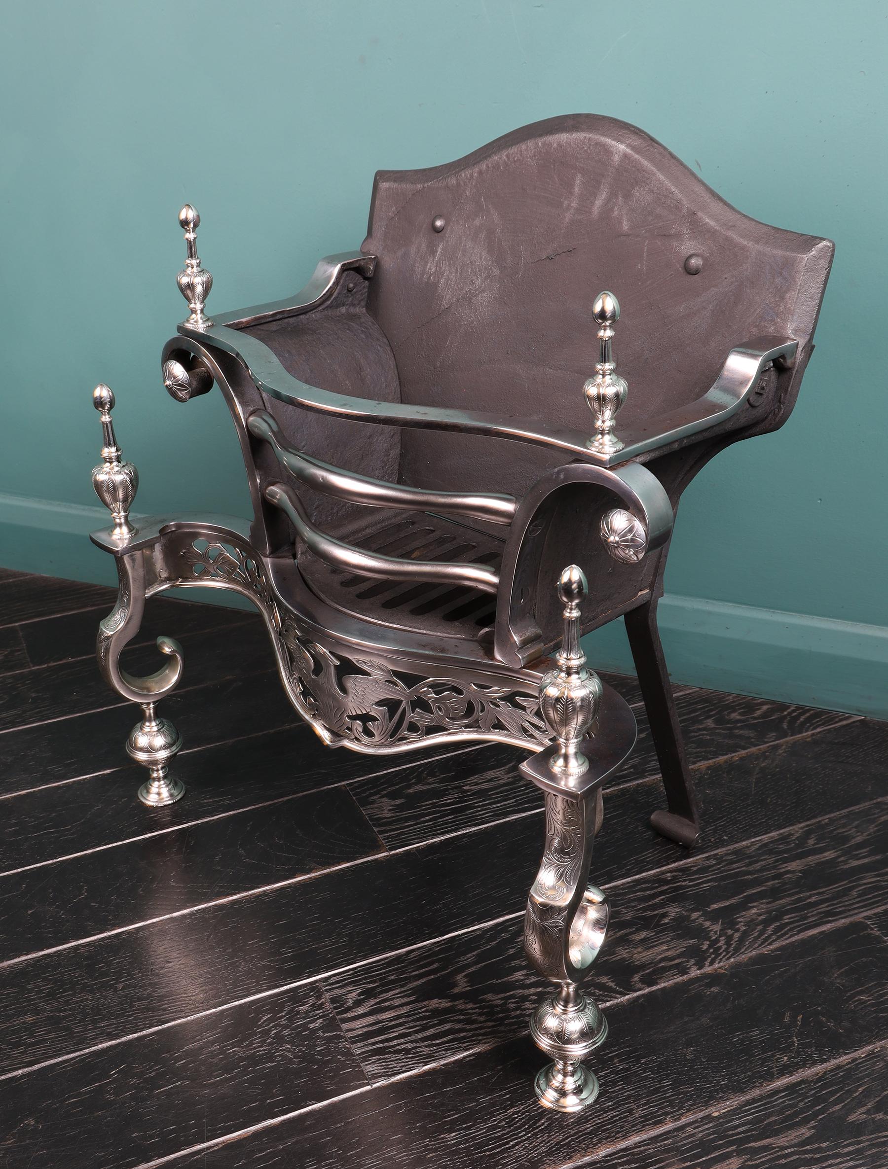 Grille de foyer anglaise en nickel et en acier, avec frette ajourée représentant un phénix central avec un feuillage environnant. Gravure fine sur les frettes, les pieds cassés et les fleurons en forme d'urne. Plaque de cheminée en fonte façonnée.