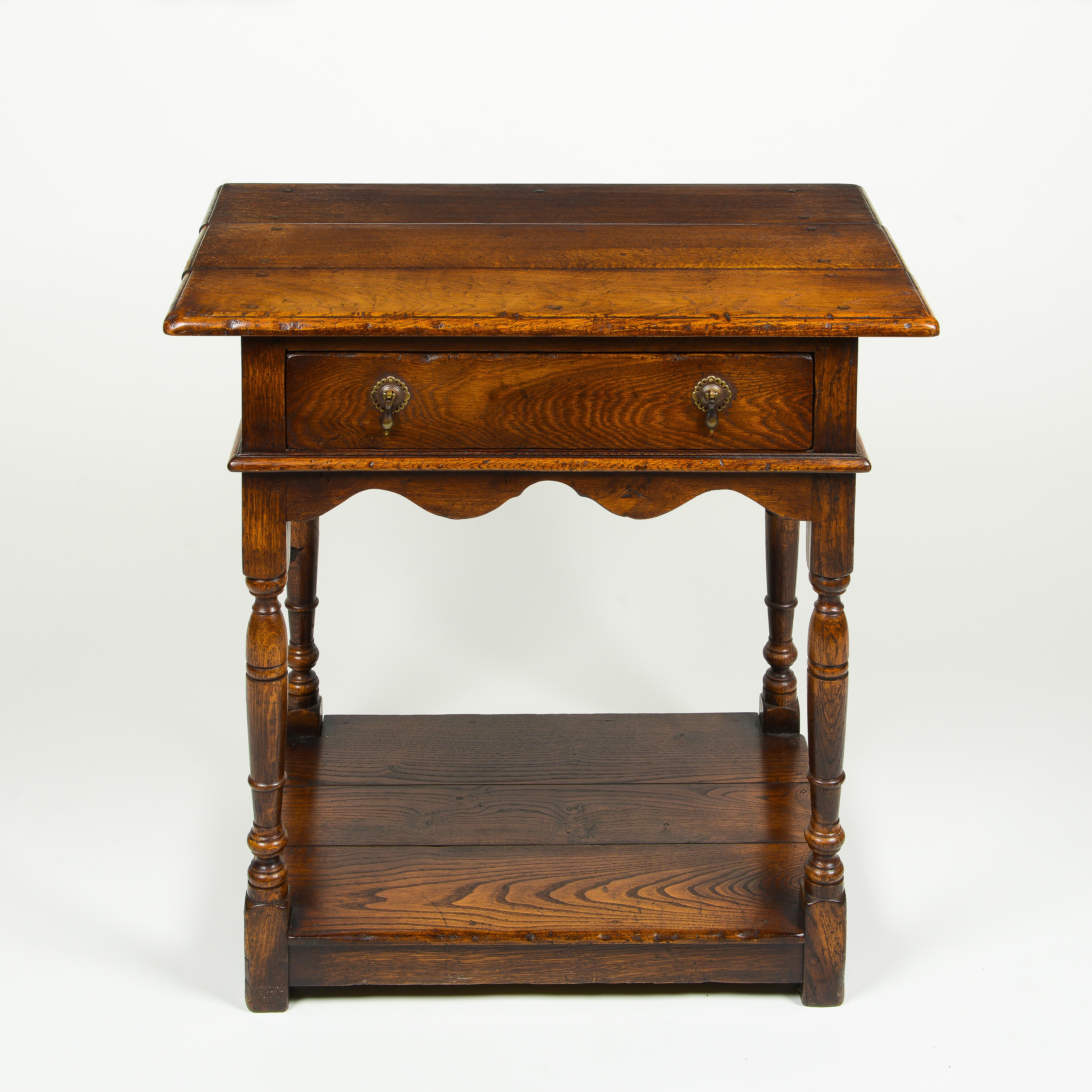 The rectangular overhanging top, above a frieze drawer mounted with original brass drop handles, and scalloped apron; raised on tapering, turned legs joined by a platform stretcher.