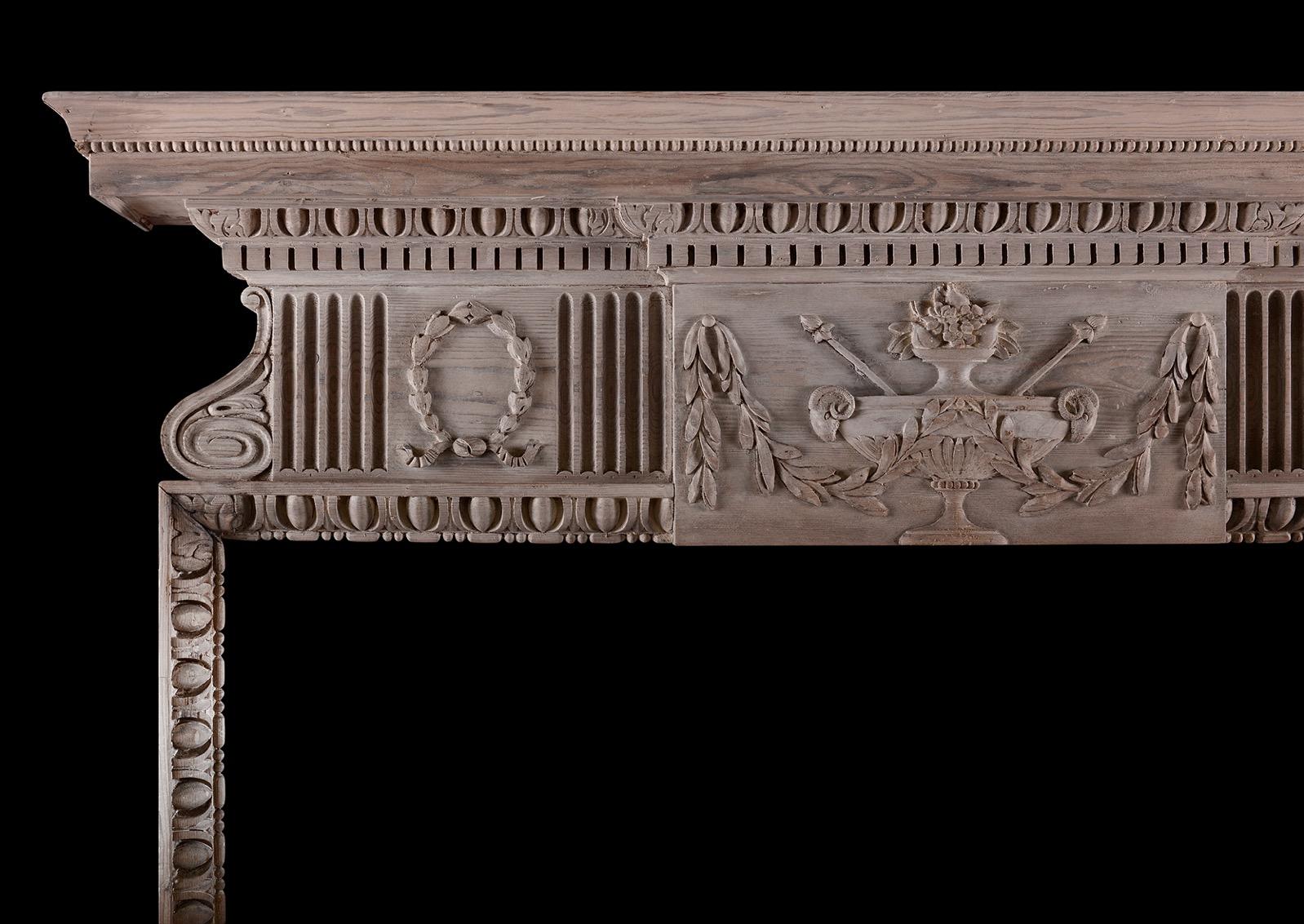 An English pine fireplace in the Georgian manner. The jambs with egg-and-dart to ungrounds, surmounted by frieze featuring centre plaque featuring urns with ram's heads flanked by flutes and wreaths. The shelf with dentils, egg-and-dart and beading.