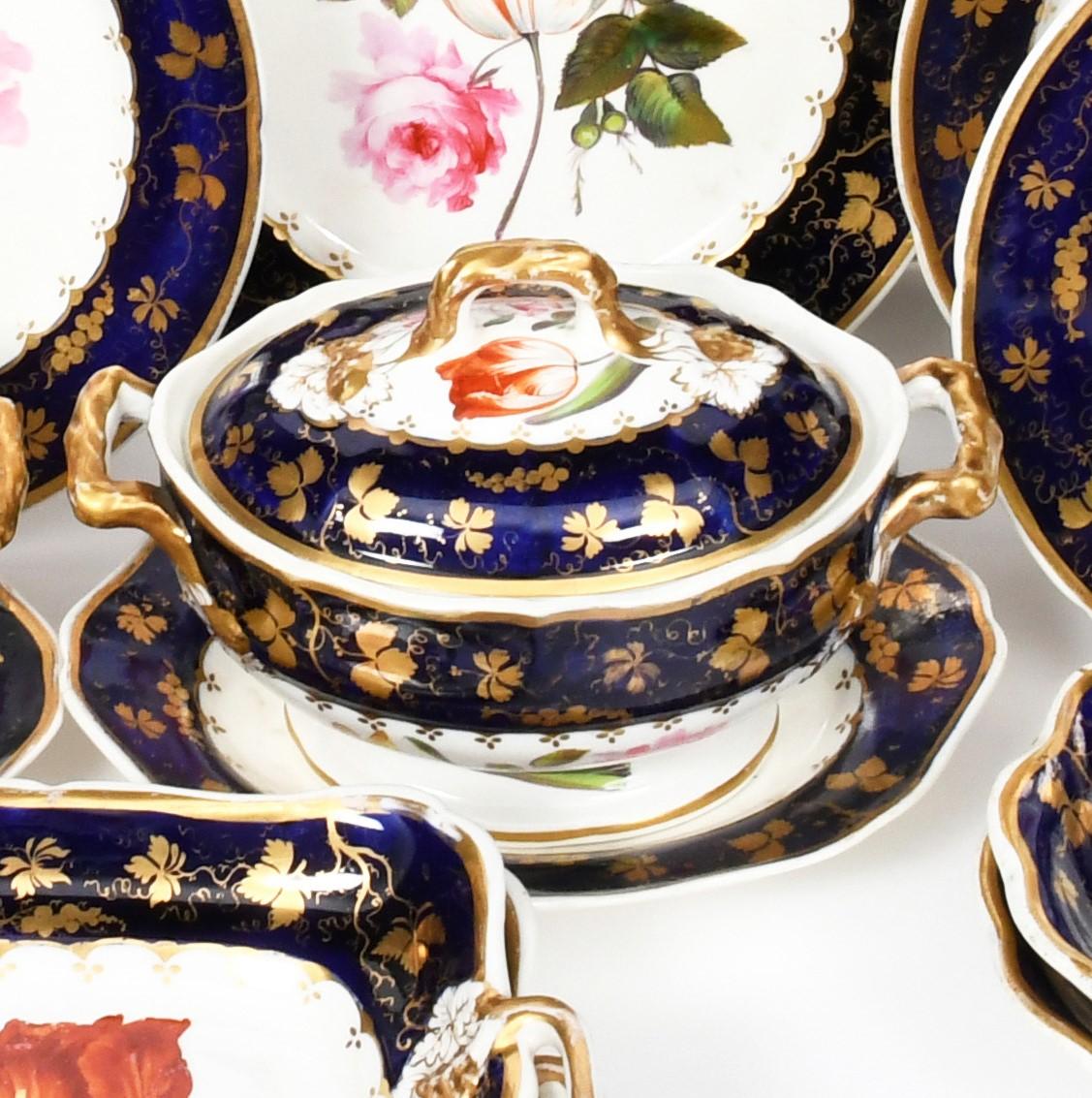 A Derby English porcelain botanical dessert service C.1820, painted with bold summer flower stems within mazarine blue borders with Gilt Grapevine. Comprising: 2 sauce tureens with covers and stands, 4 shell-shaped dishes, 2 square dishes, 1 oval