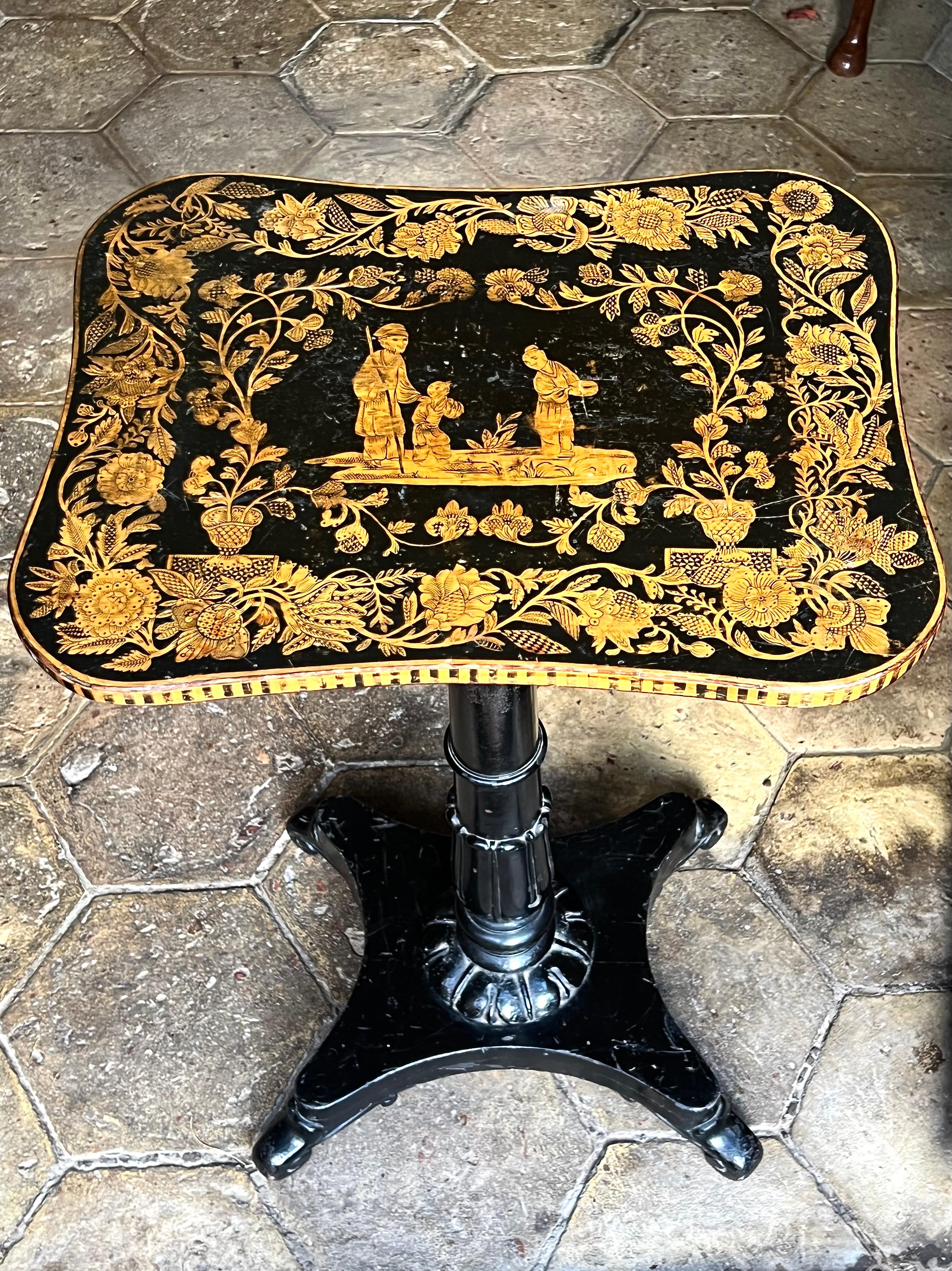 Table d'appoint en chinoiserie de la période Regency anglaise, vers 1815.

Le plateau rectangulaire inhabituel en forme de serpentin doux est abondamment décoré et centré par une scène de chinoiserie représentant un homme, une femme et un enfant,