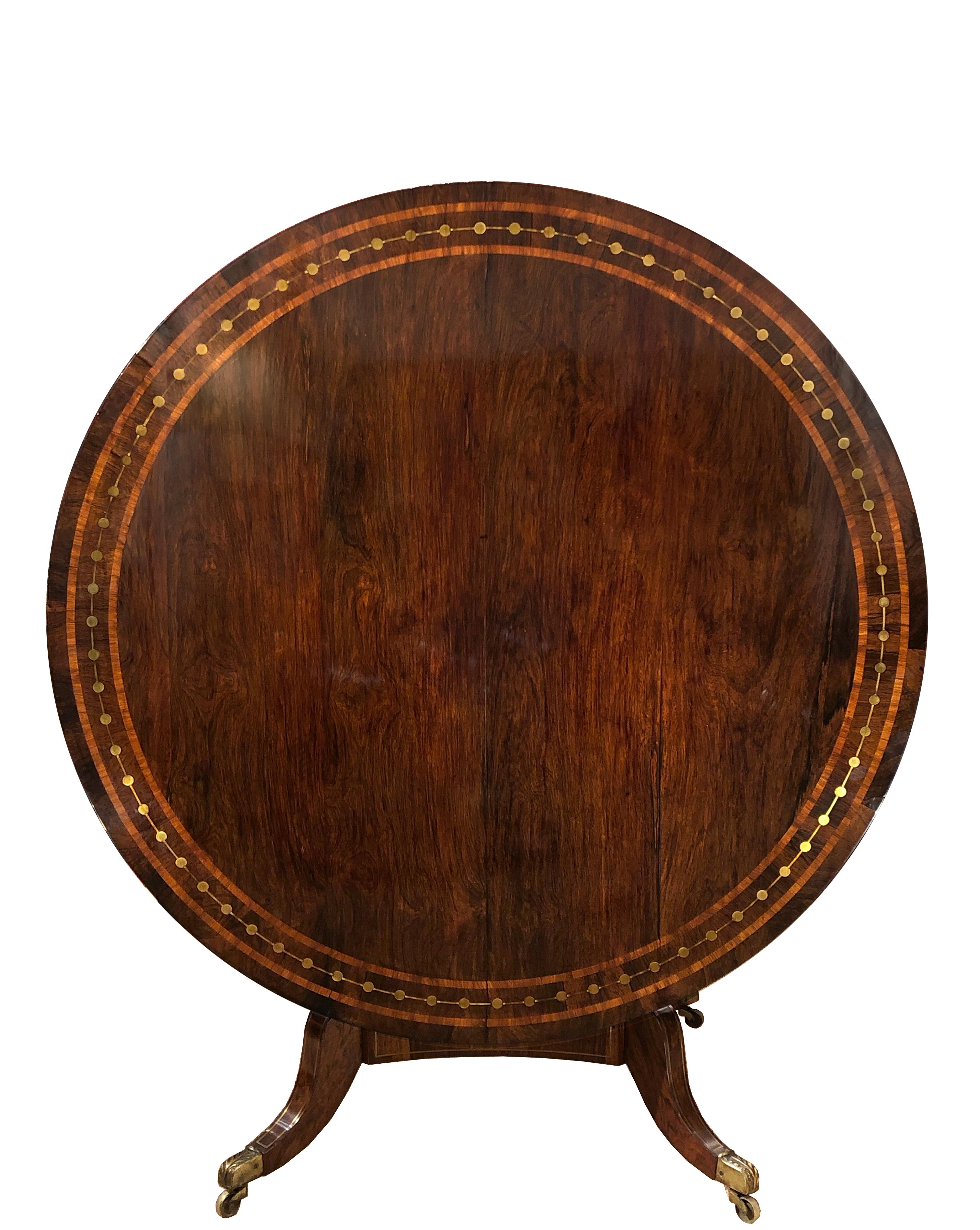 A Regency period rosewood tilt-top table
Rosewood veneer with satinwood banding to top; brass inlay to the top, apron, base and legs, with its original brass casters. For use as dining, breakfast, games, or center table.
England, circa 1820.
  