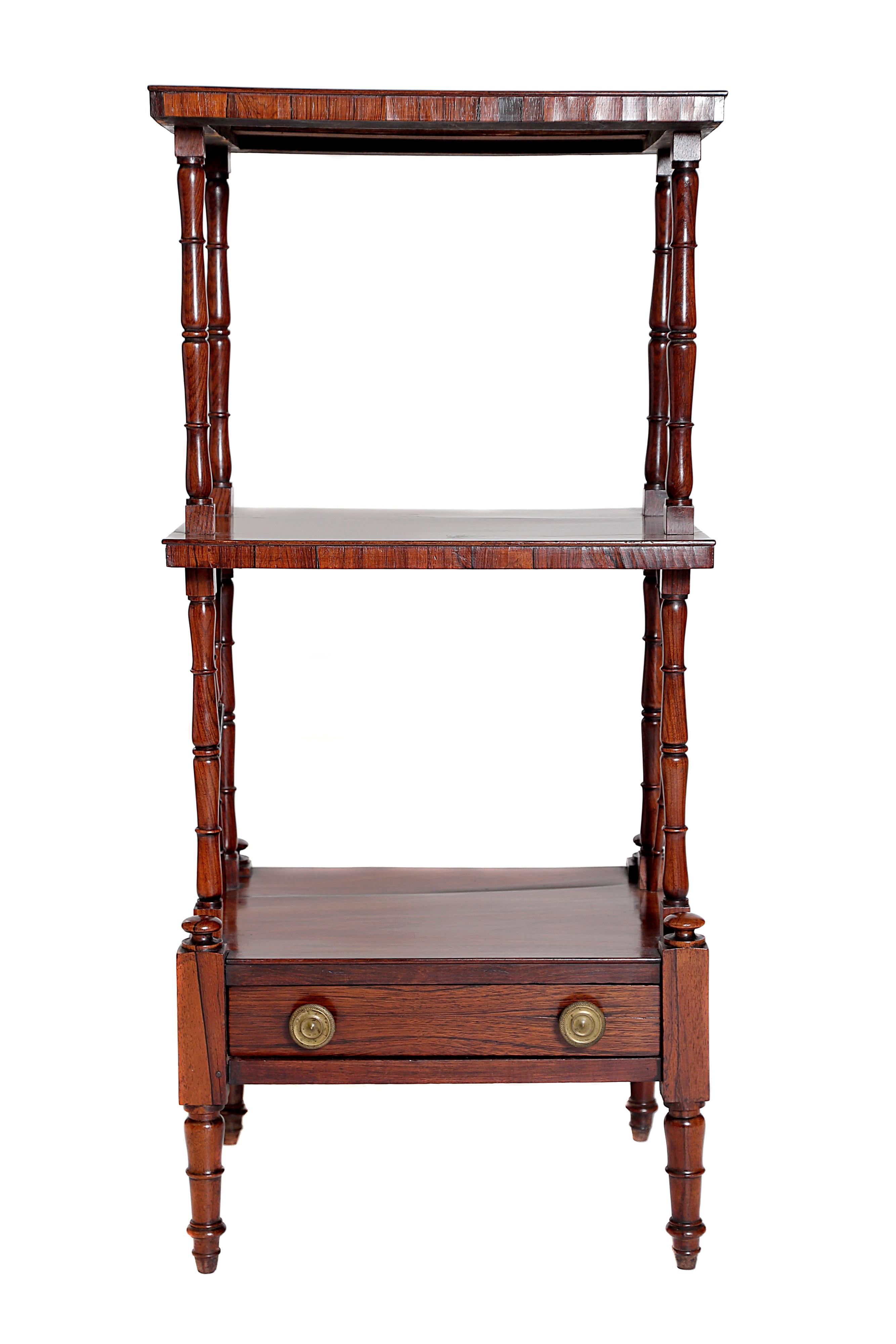 An English Regency rosewood 3-tier whatnot / bookshelf. Handmade of rosewood, with great color and patina. Three tiers, supported by turned columns with lovely turned spindles in between. A single drawer to the base, cup castors missing.