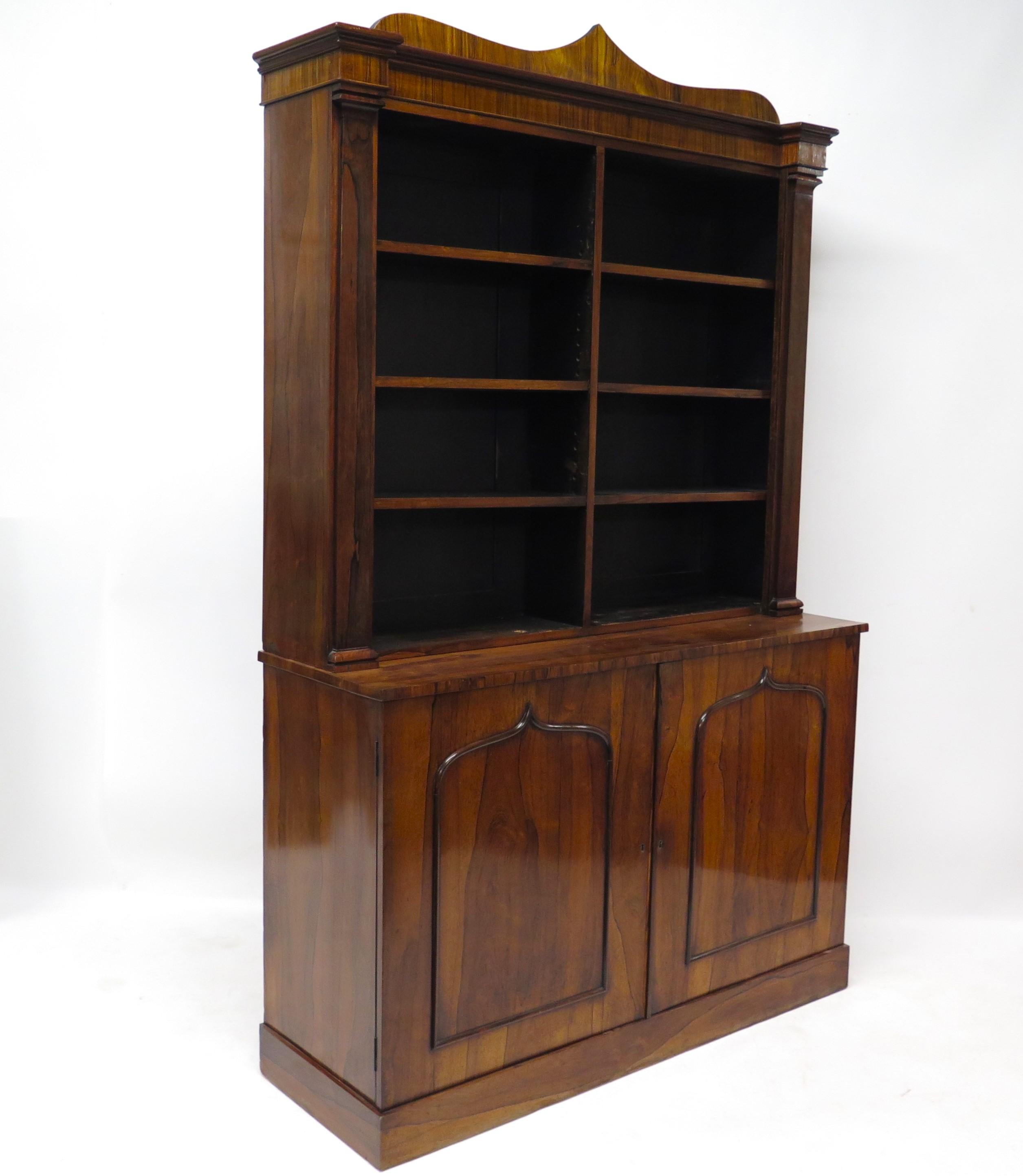an English Regency rosewood bookcase with shelves at the top and two doors at the bottom, curved top with point in center, trim on doors echoes it, pilasters at sides of top portion. England. Circa 1820.

( TWO AVAILABLE )  

MEASUREMENTS:

86
