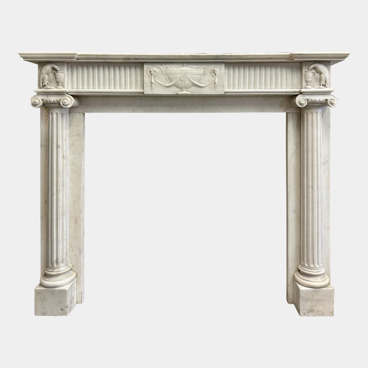 A very good quality English Regency period fireplace executed in Italian Statuary white marble. The jambs with fluted columns stood on square foot blocks with carved Ionic capitals, with scrolled facia and acanthus leaf within. 
The corner blocks