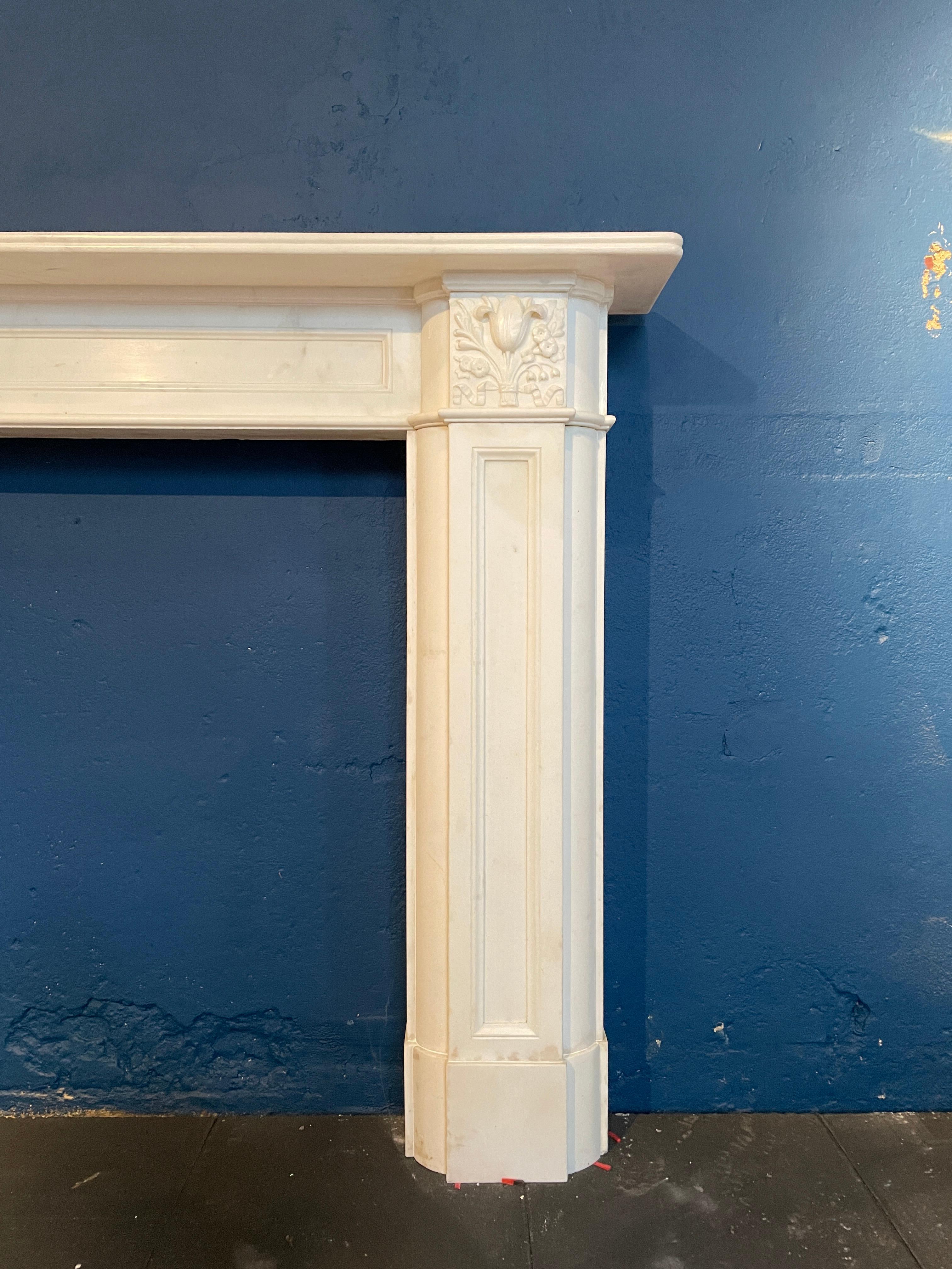 A large and well proportioned Regency fireplace in Statuary white marble. The panelled jambs with cushioned side returns stood on separate foot blocks and surmounted by carved foliate end blocks. The frieze with conforming panelled design, all