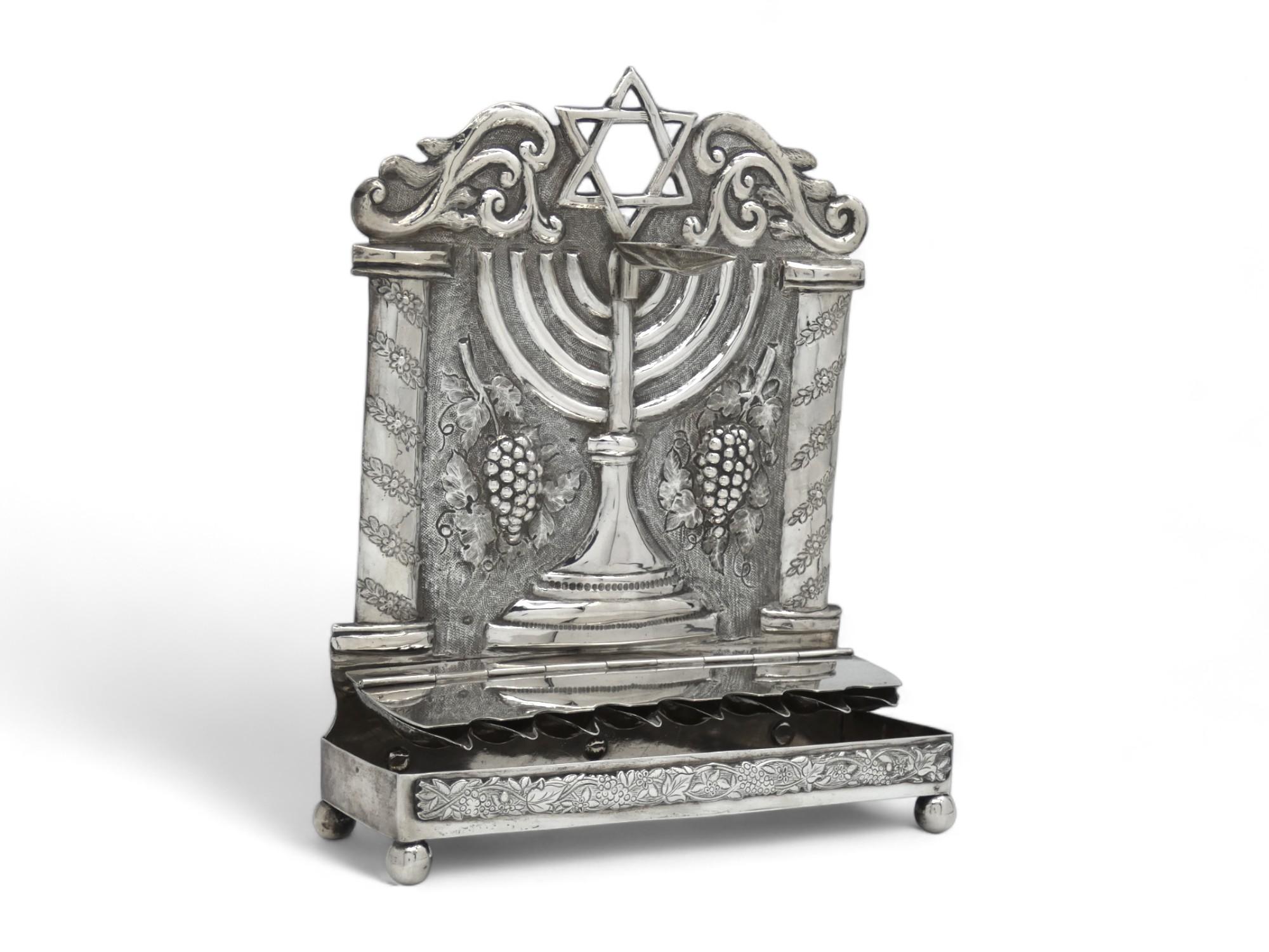 Una lampada di Hanukkah mozzafiato realizzata nei Paesi Bassi alla fine del XIX secolo.

La piastra posteriore presenta una grande menorah con una base a gradini e una lunga lampada ovale staccabile applicata alla sua sommità.

La Menorah è