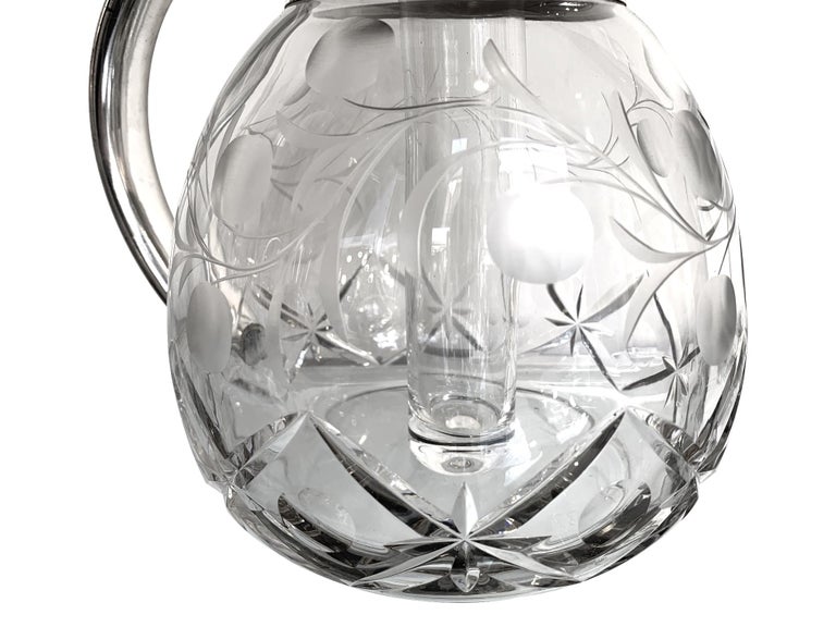 An English silver plated crystal lemonade / cocktail jug engraved with leaf and branch motif with circles. Mounted with a hinged silver plated lid and handle that opens to reveal the central glass ice compartment, with ring pull top.