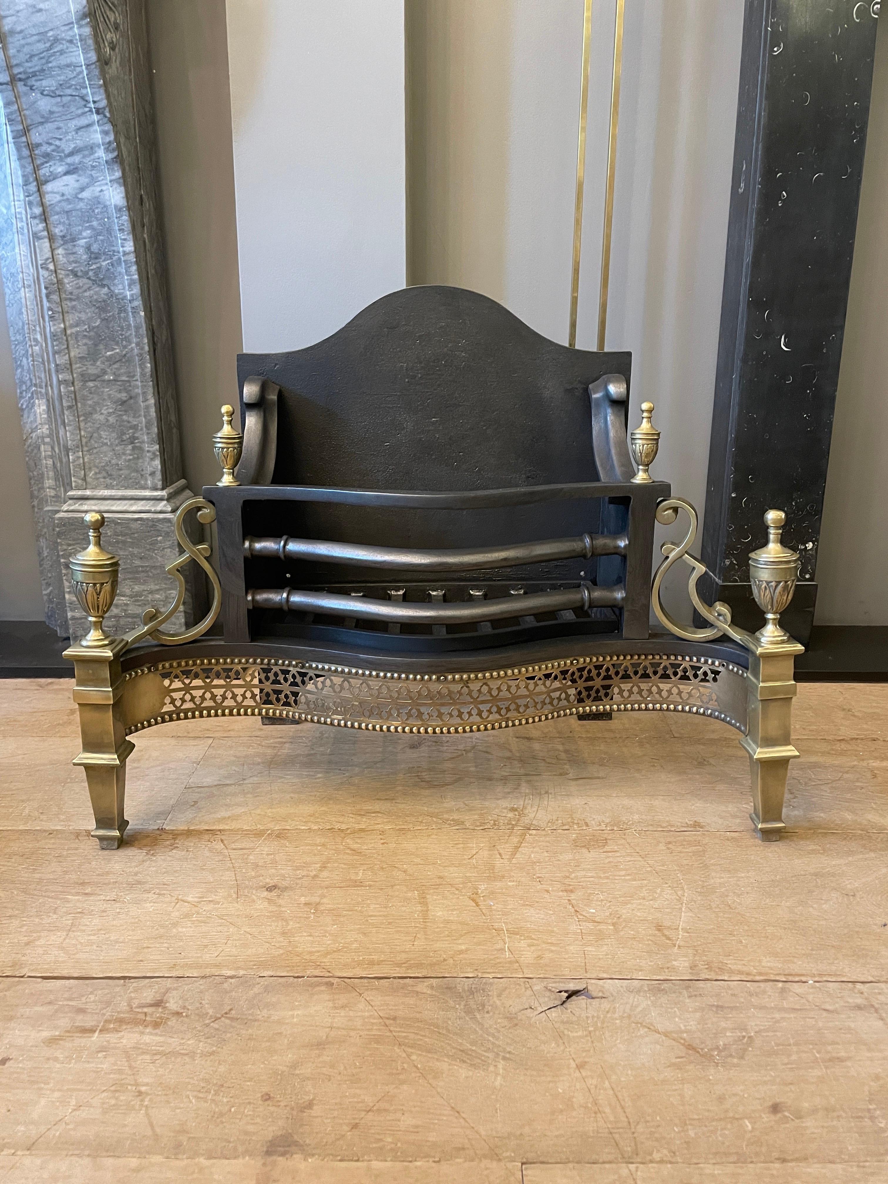 A good quality English brass and steel fire grate. The pierced brass fret surmounted by shaped burning area which is flanked by brass scroll work. The legs surmounted by decorative brass finials. Shaped cast iron back behind. 20th century.
