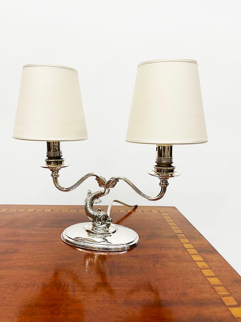 An English sterling silver dolphin 2 arms table lamp

An English silver dolphin 2 arms table lamp with 2 loosely clamped lampshades.
On an oval base a dolphin fish with 2 curled arms from the tail, each with a lamp fitting (numbered with nr.