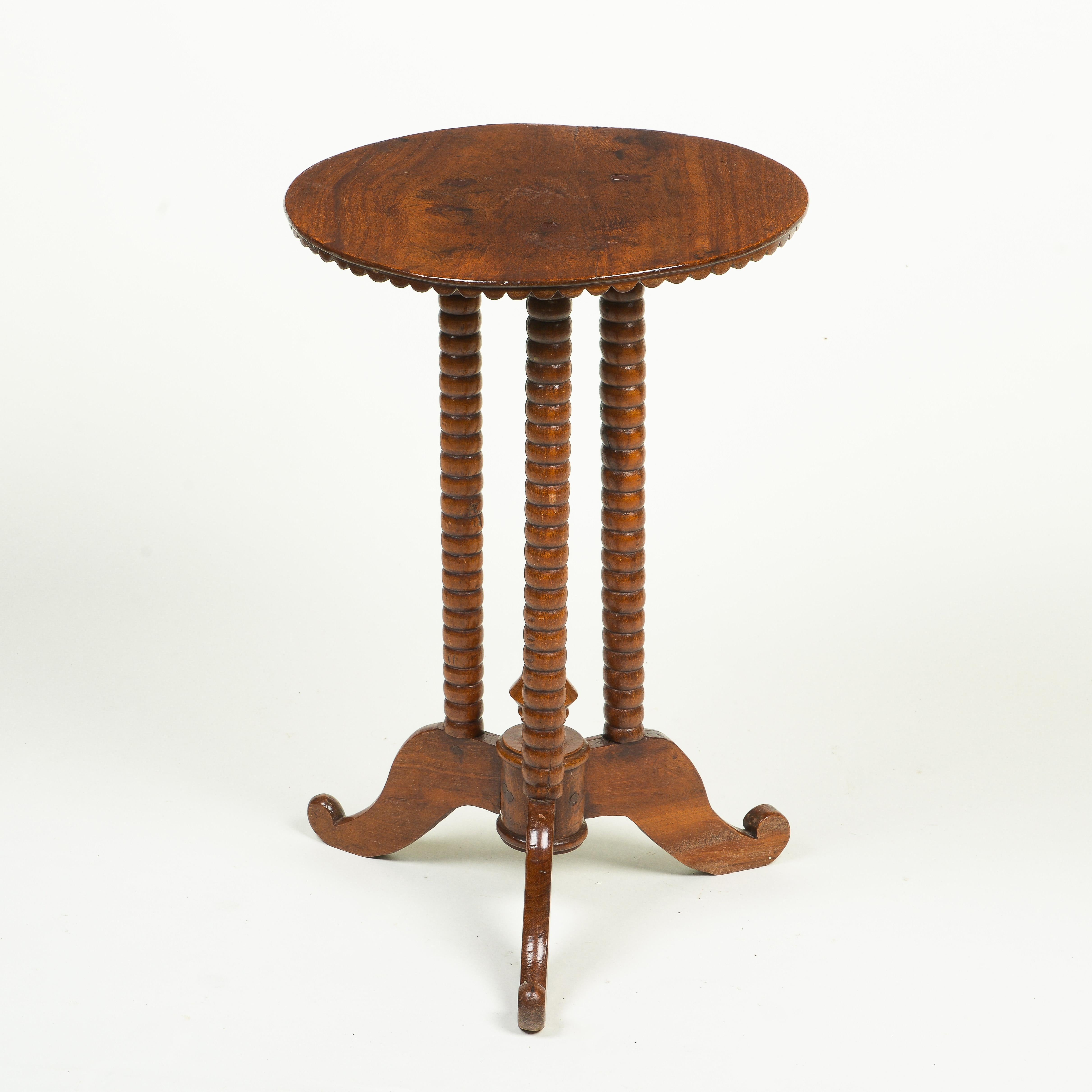 The round top with with scalloped edge; raised on three bobbin turned supports on downswept scrolling feet centered by an arrow-form finial.