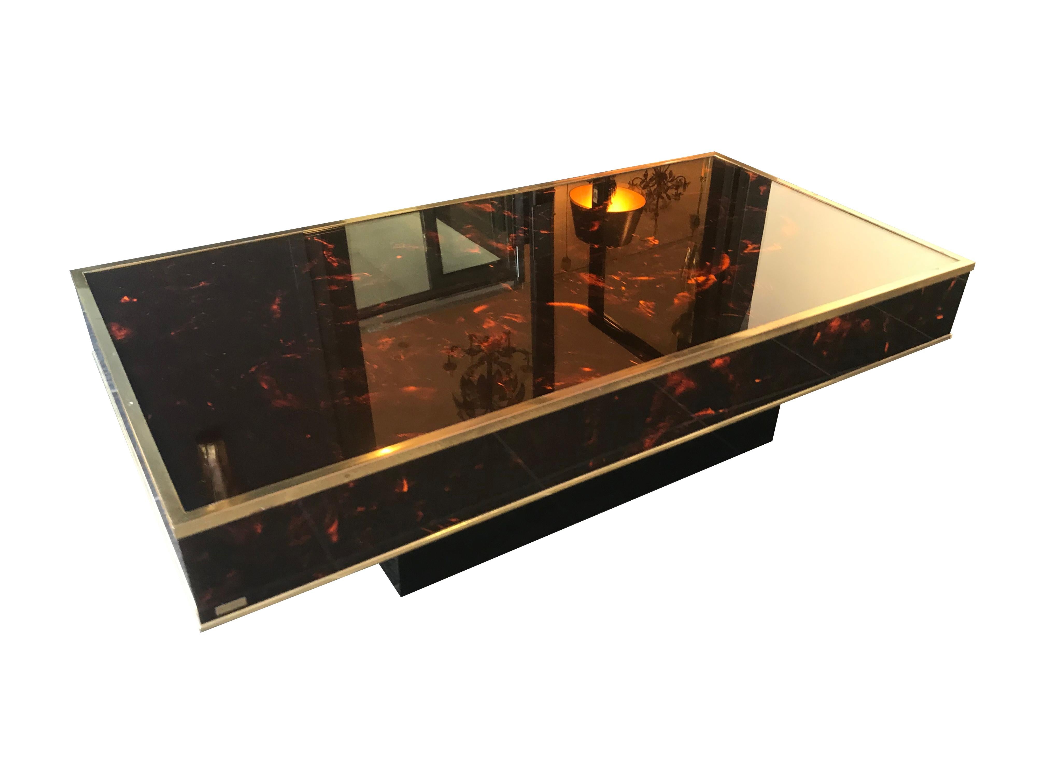 An Eric Maville faux tortoiseshell coffee table with clear glass top and gilt metal edging, mounted on a black laminated base. With brass plague stamped 