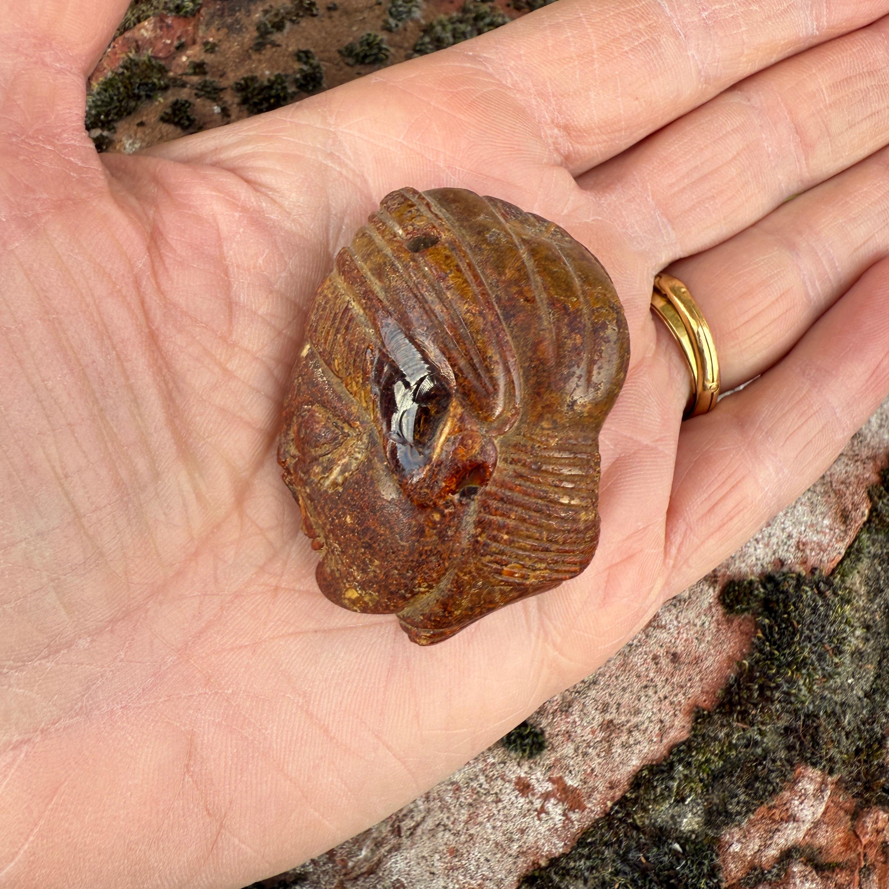 An Etruscan Amber Head Pendant.
 
Etruria, circa 5th century B.C.
 
Measurements
5.1 × 3.6 × 2.4 cm.
 
9cm high on its bronze display stand. 
 
Provenance
Anonymous sale; Sotheby’s London, Antiquities, 14–15 December 1981, lot 206.
The property of