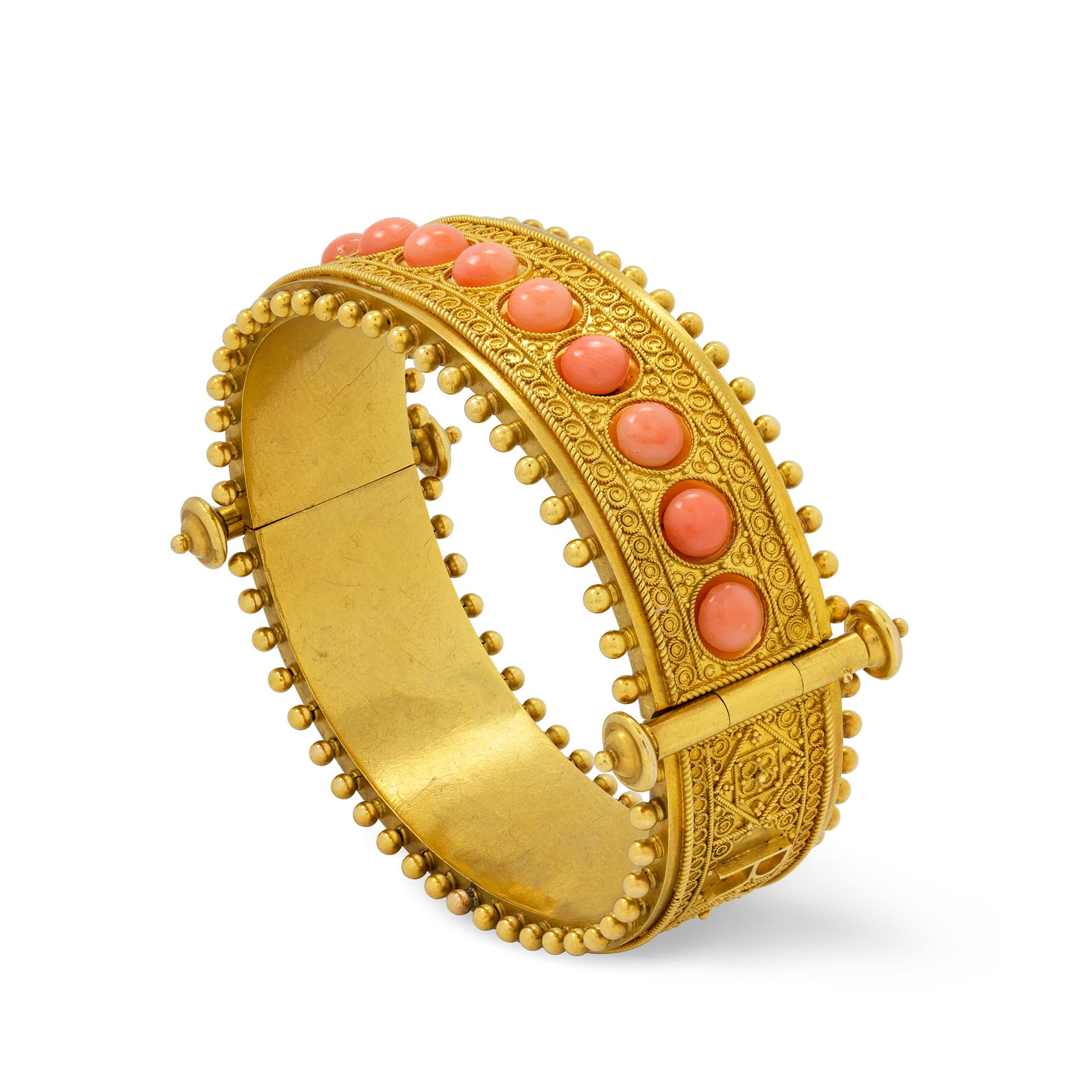 An Etruscan Revival gold and coral hinged bangle, set to the one side with twelve cabochon-cut corals, surrounded by wire-work decoration of geometric design, the other side with wirework of similar design, applied the motto 