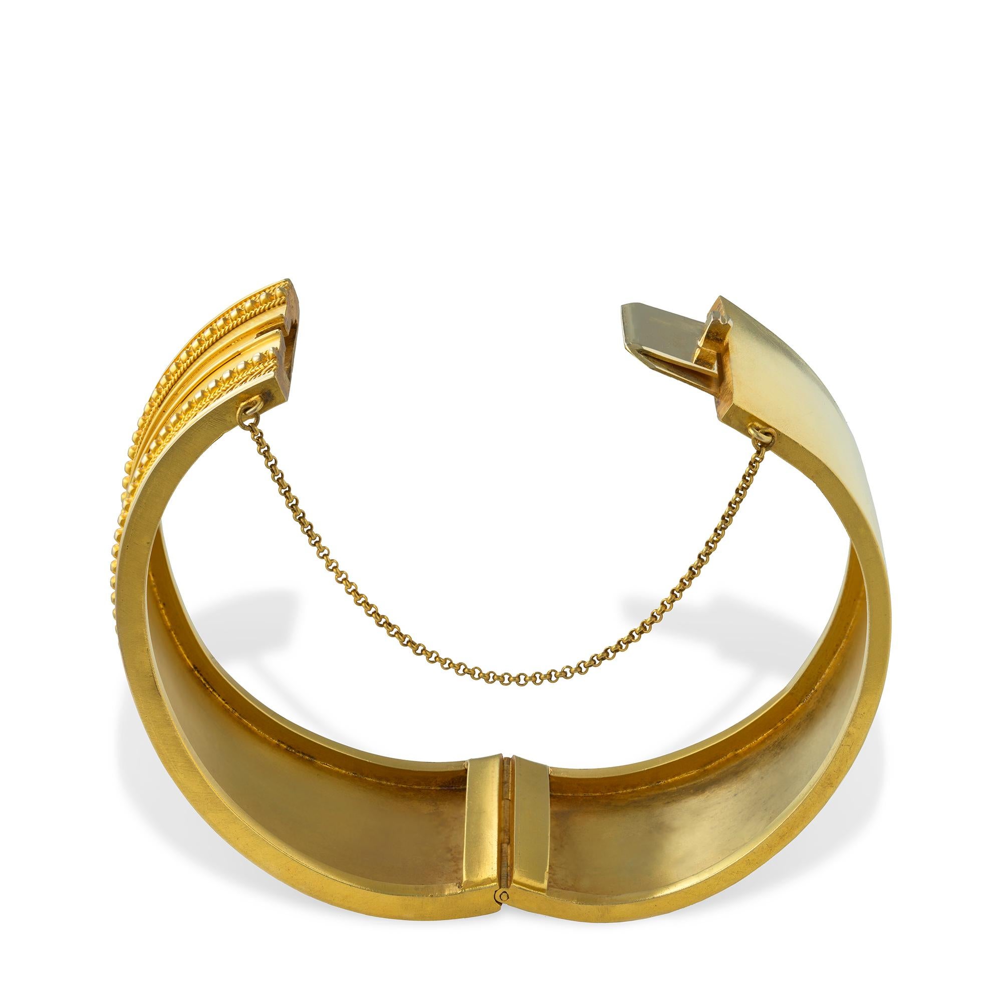 An Etruscan Revival yellow gold bangle, the front bordered by Etruscan style design with granulation to a plain gold back and concealed hinged clasp with safety chain, circa 1870,measuring internally  5.5 x 4.9cm, gross weight 32.5 grams.

This