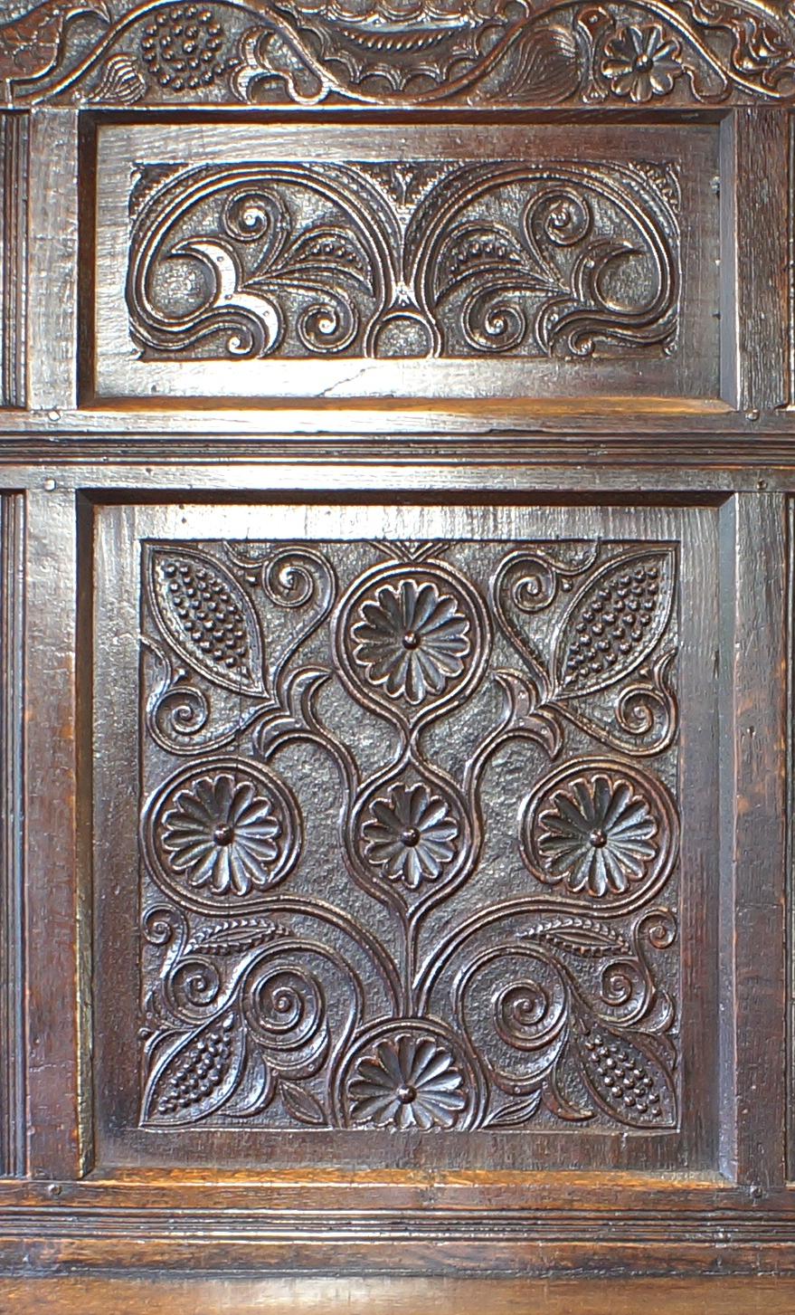 A truly magnificent carved 17th century settle of a grand and imposing size.
The top rail caved with scrolling vine leaves, peacocks, flowers and seed pods.
Four landscape panels above four portrait panels all carved with stylised flowers, leaves