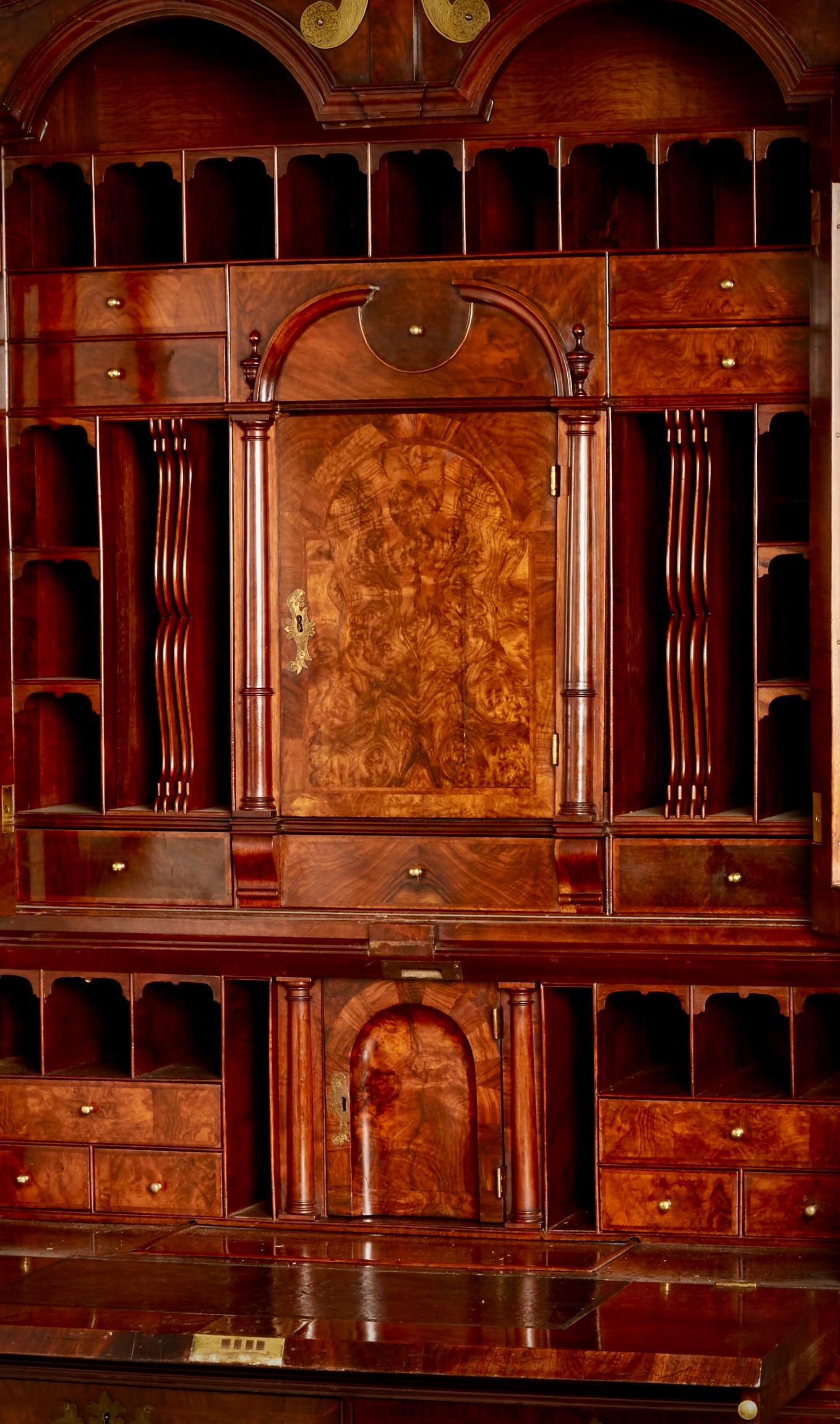 El frontón de cuello de cisne flanquea una urna torneada y acanalada, coronada por cuatro remates de urna adicionales, sobre puertas de doble cúpula con cristal biselado posterior que encierran un interior totalmente equipado con cajones, agujeros