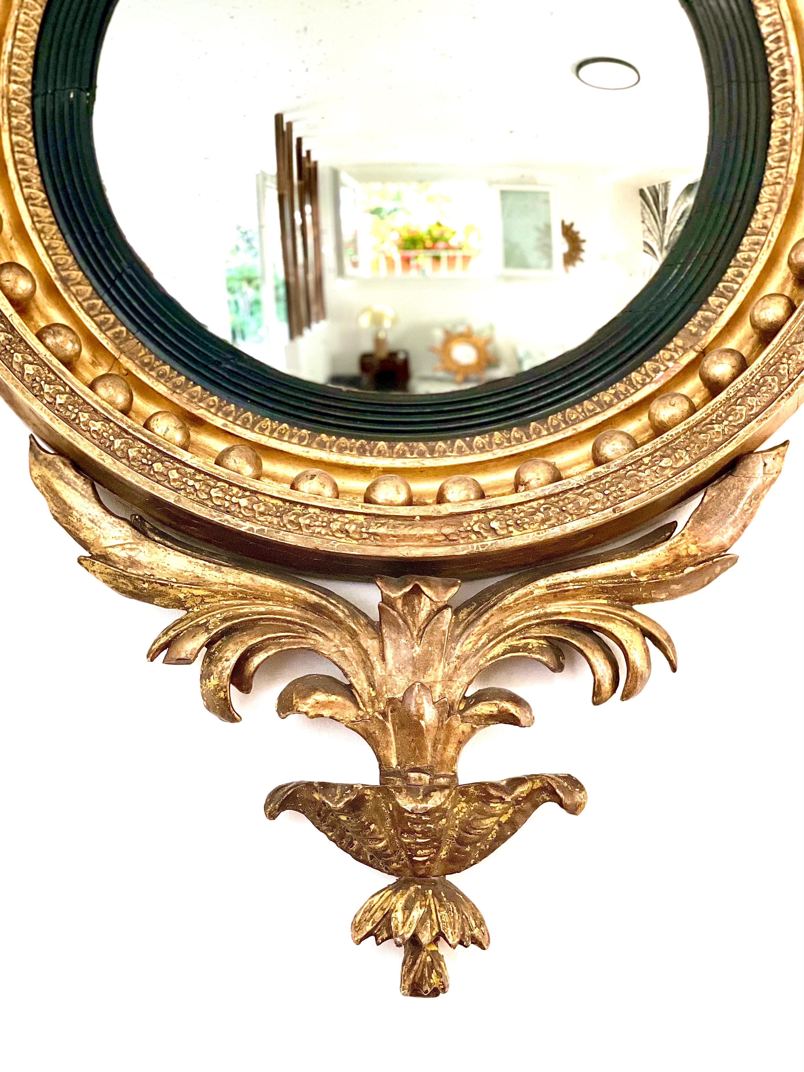 This very fine Regency convex mirror is dating from the early 19th century, it is made of giltwood and blackened stucco. This exceptional and rare Regency mirror is topped with a giltwood eagle with outstretched wings, flanked on each side by