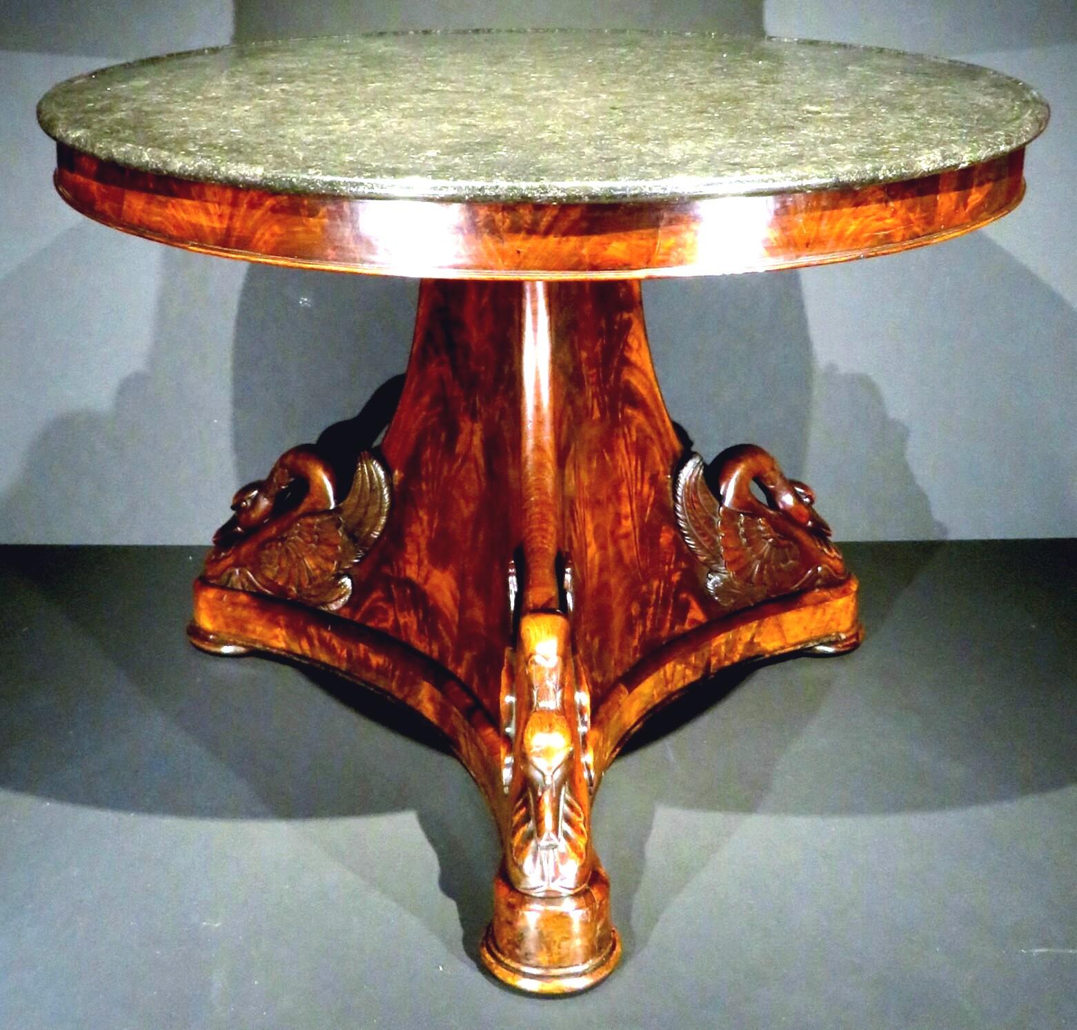The original fossilized black marble circular top over a conforming frieze of richly figured crotch mahogany, mounted upon a stunning flame-mahogany tri-corner base accented with three individual hand carved & applied swan-shaped elements, raised