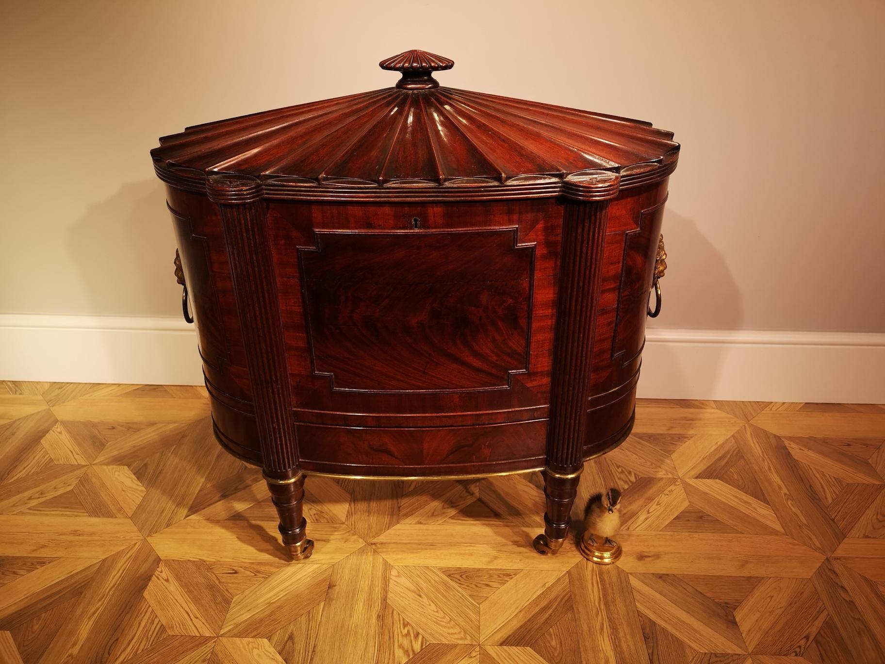 An exceptional George III mahogany cellaret of oval form with a superb radially fluted hinged lid centred by a stylised fluted finial,  edged by a reeded border with inset carved paterae to the top of the four projecting reeded columns, the whole