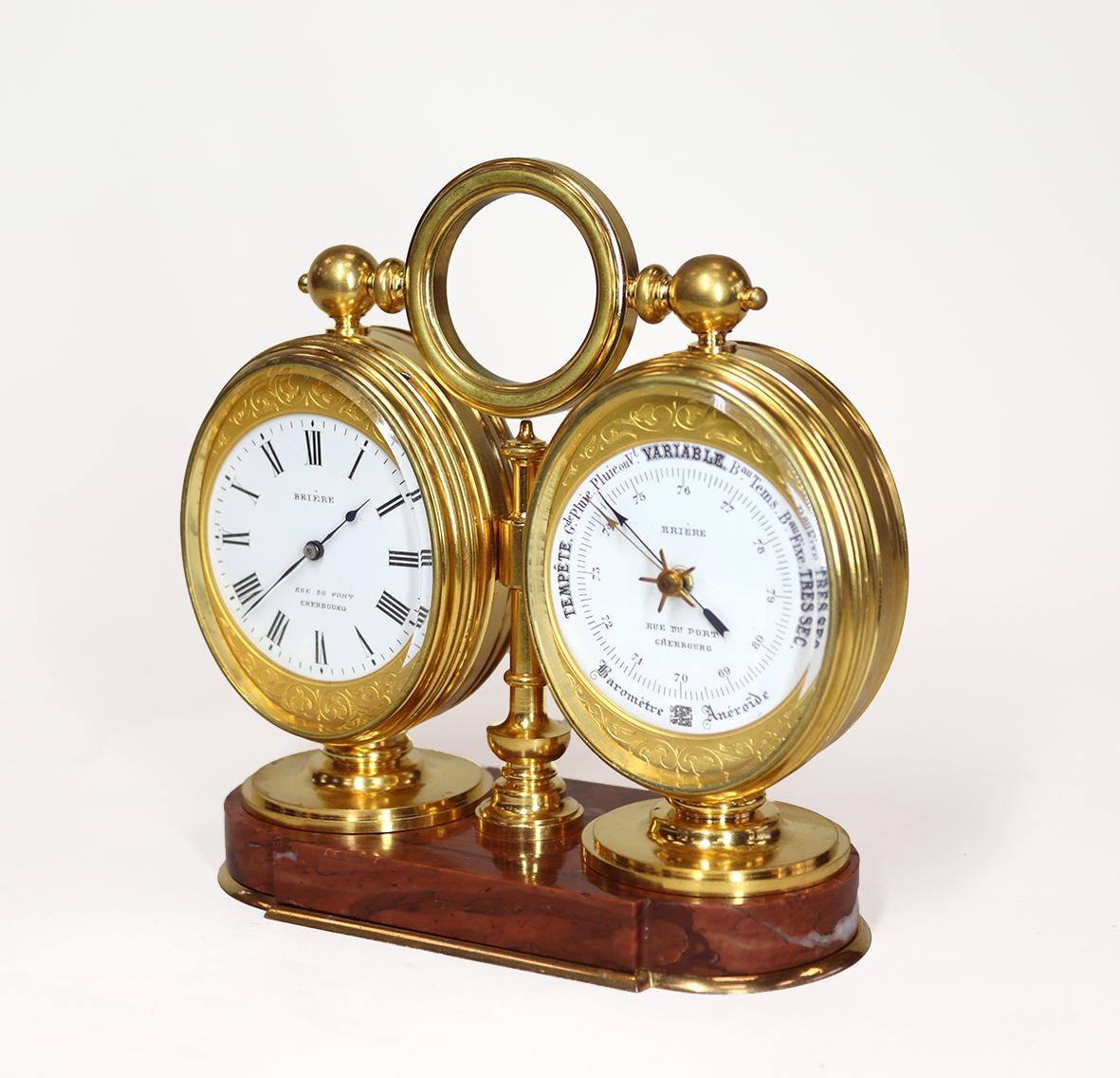 A very fine desk compendium, comprising an eight day timepiece, barometer and thermometer, in a gilded twin oval case, mounted on a rouge marble base with a rotating circular carrying loop.  The reverse has a glazed back to the clock revealing an
