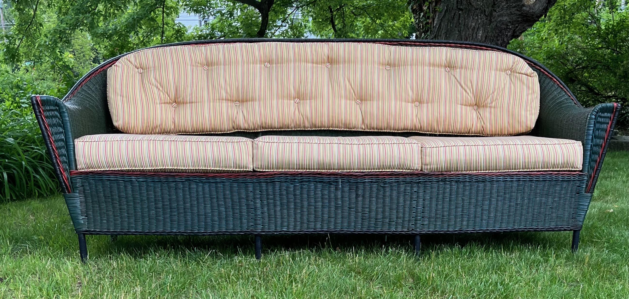 A beautiful large scale rounded top, closely woven designed and fully skirted three seat wicker sofa. A sofa that makes a statement in a room or porch ! It is painted in a handsome dark green finish with cranberry red and black accent trimming