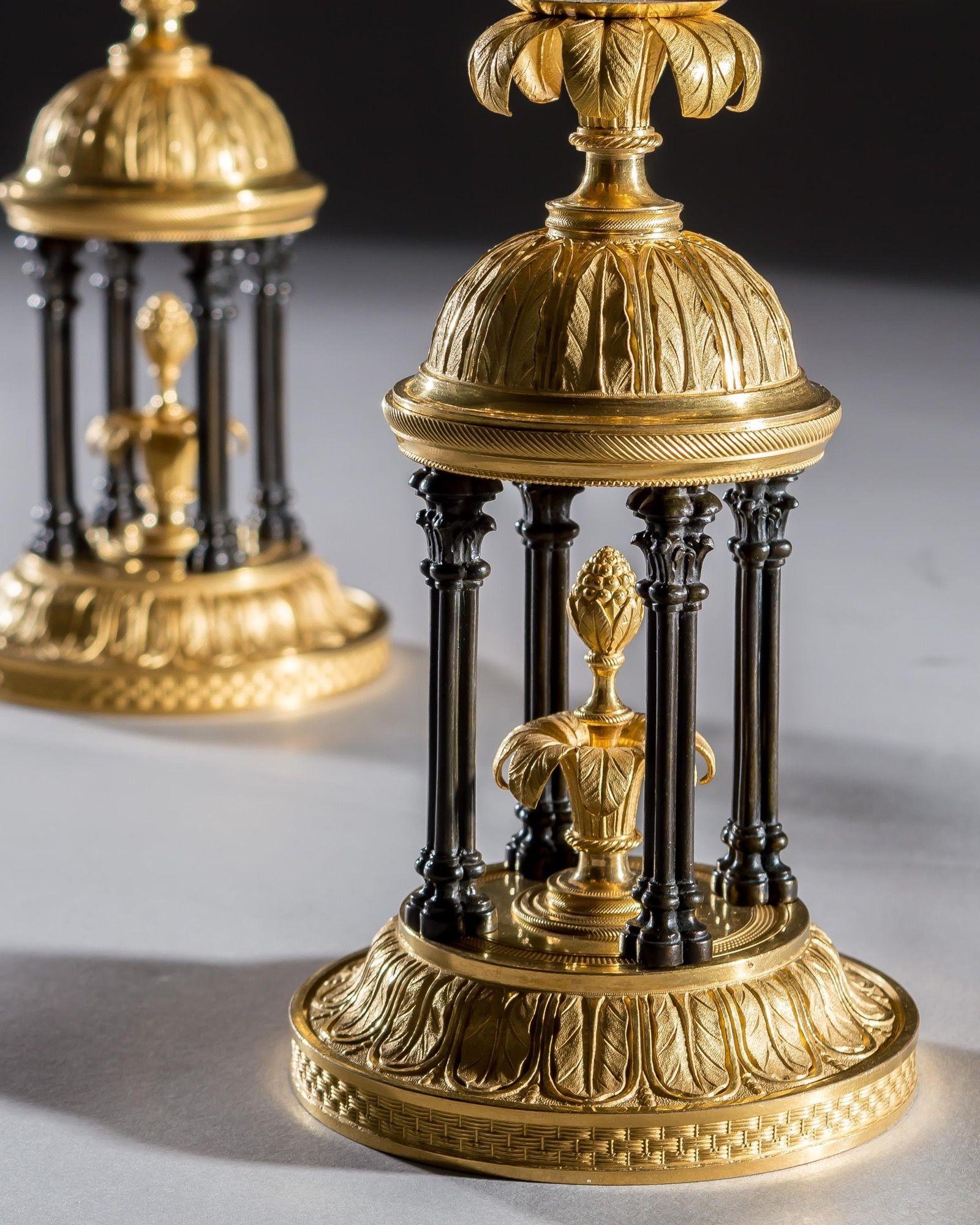 A exceptional pair of candelabra of temple form, the finely chased ormolu bases with basket weave band and foliate decoration supported on bronze columns, issuing twin scroll arms fitted with candle nozzles and drip pans, the central column with