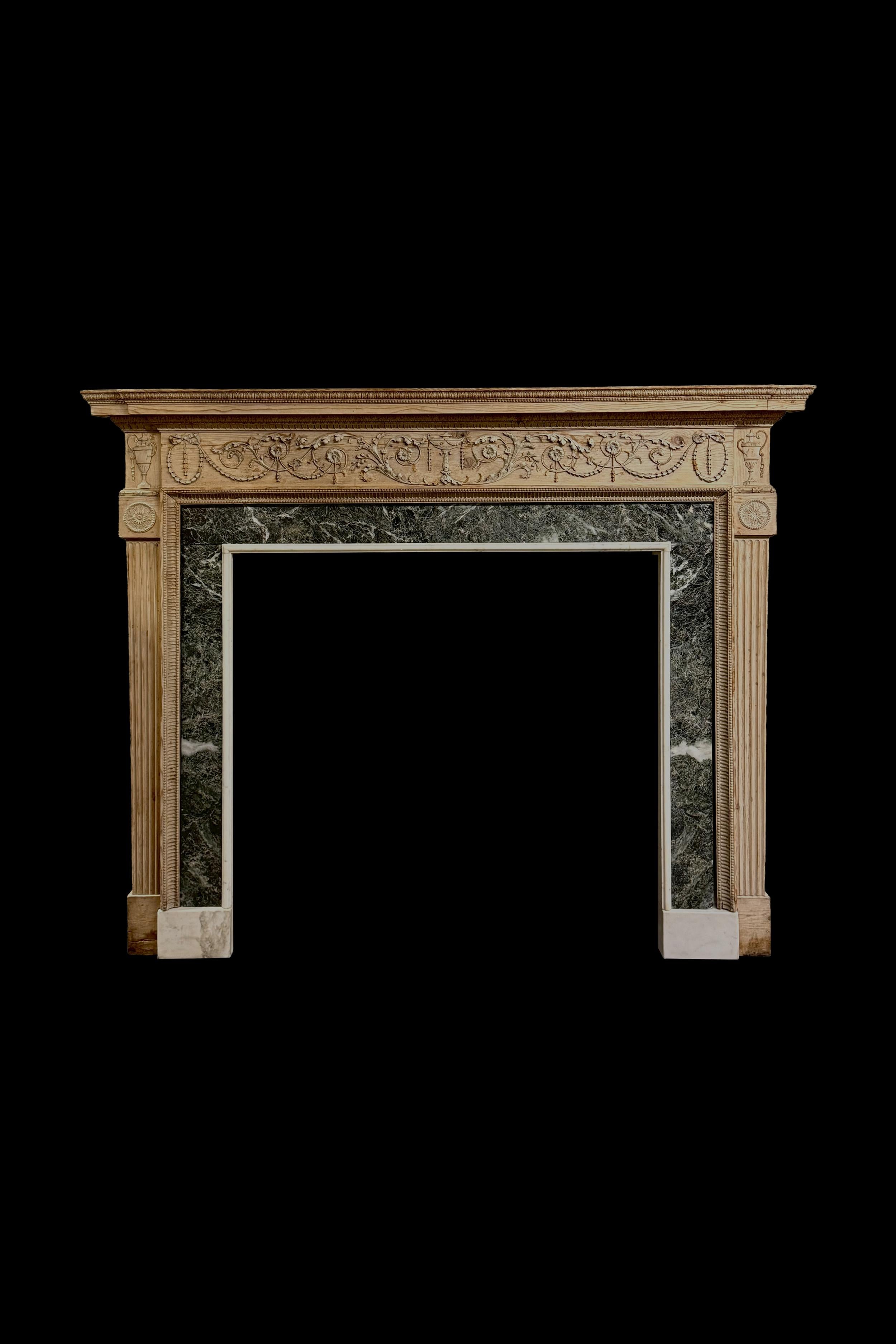 An exceptionally fine Neo-classical pine chimneypiece with original Verde Antico marble slips with a frieze carved in fine low relief centred with an urn flanked by foliate arabesques and ribbon tied bell drop swags, the aperture framed by a