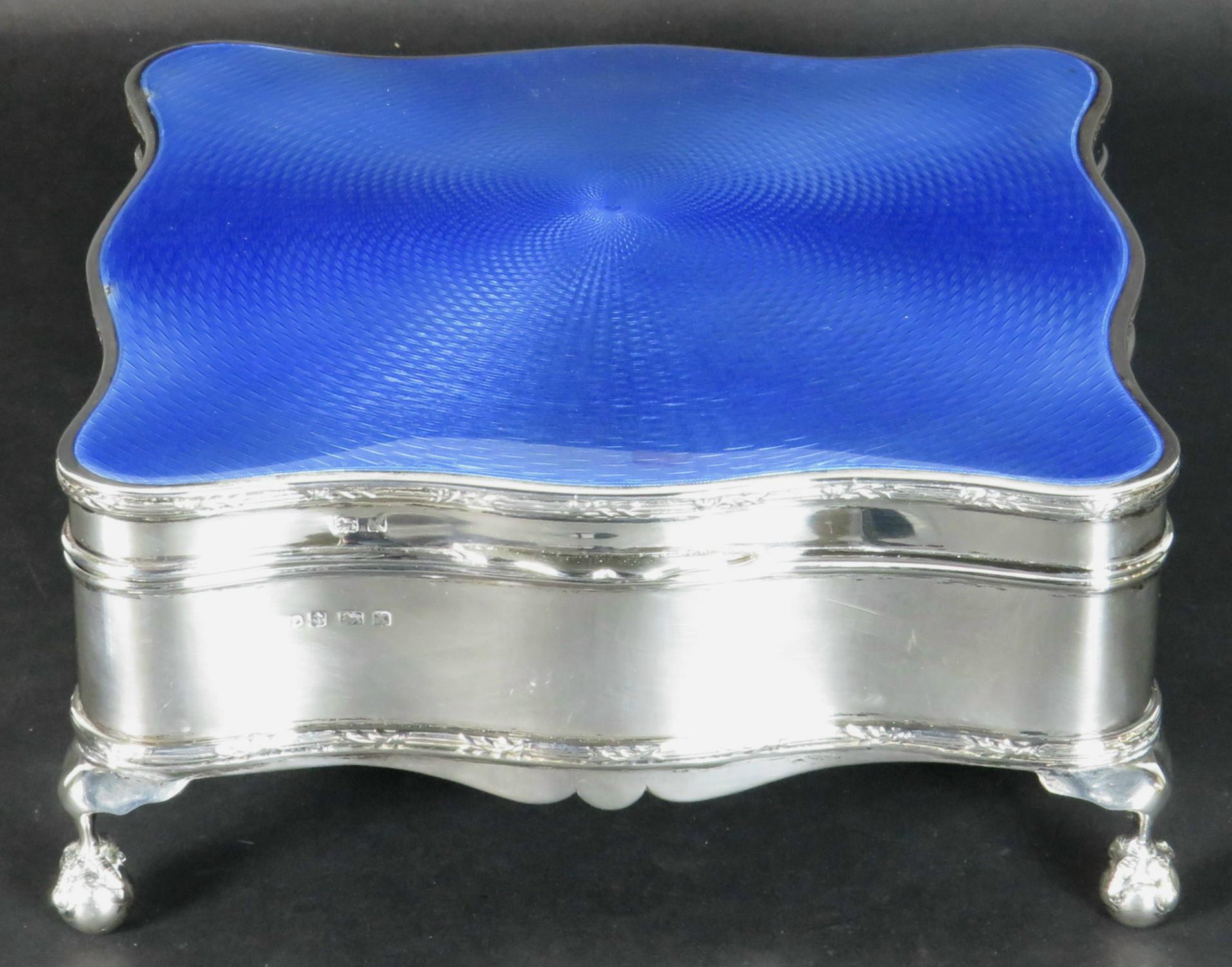 A fine and exceptionally large English Art Deco sterling silver & enamel jewelery box. The serpentine-shaped case fitted with a conforming hinged lid decorated in striking powder-blue enamel with radiating interwoven machined motifs, opening to an