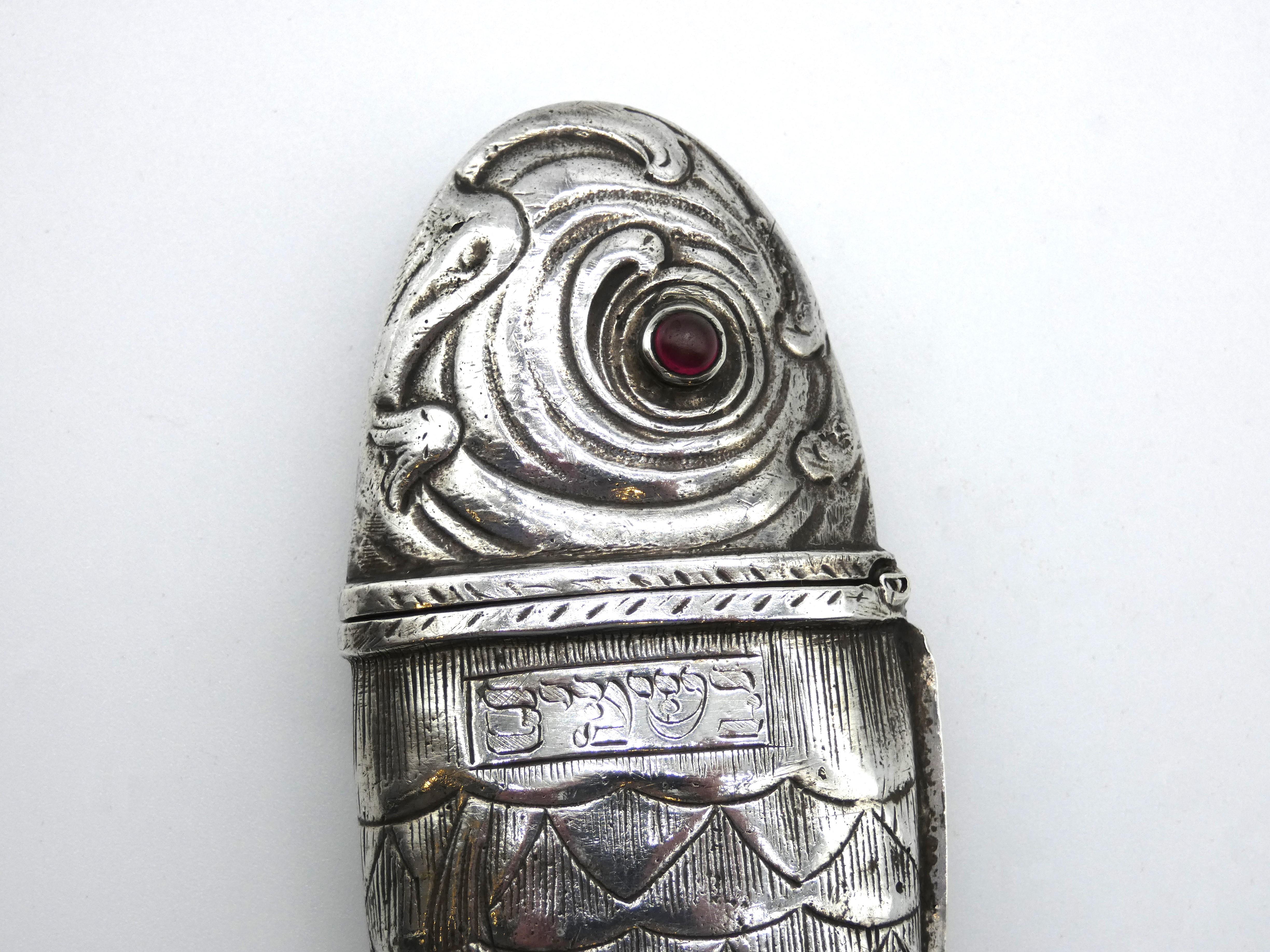 Head of spice container is designed in an oncoming wave pattern with two ruby colored gemstone eyes. Hinge set at neck for easy opening to refill spices. Decorated with elegant moving scales along the body. Marked at tailfin. Hebrew inscription