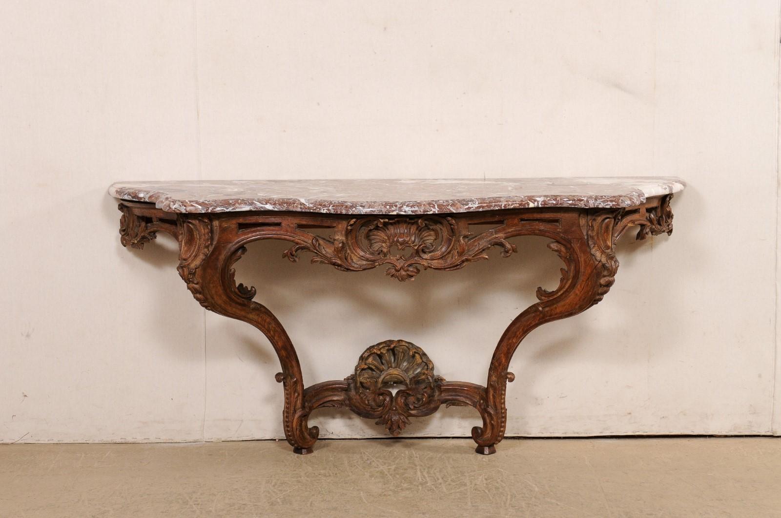 A French elaborately-carved wall console with marble top from the 18th century. This antique table from France, which retains its original serpentine-shaped marble top (with flattened backside), has a wood frame with an exquisite rocaille aesthetic