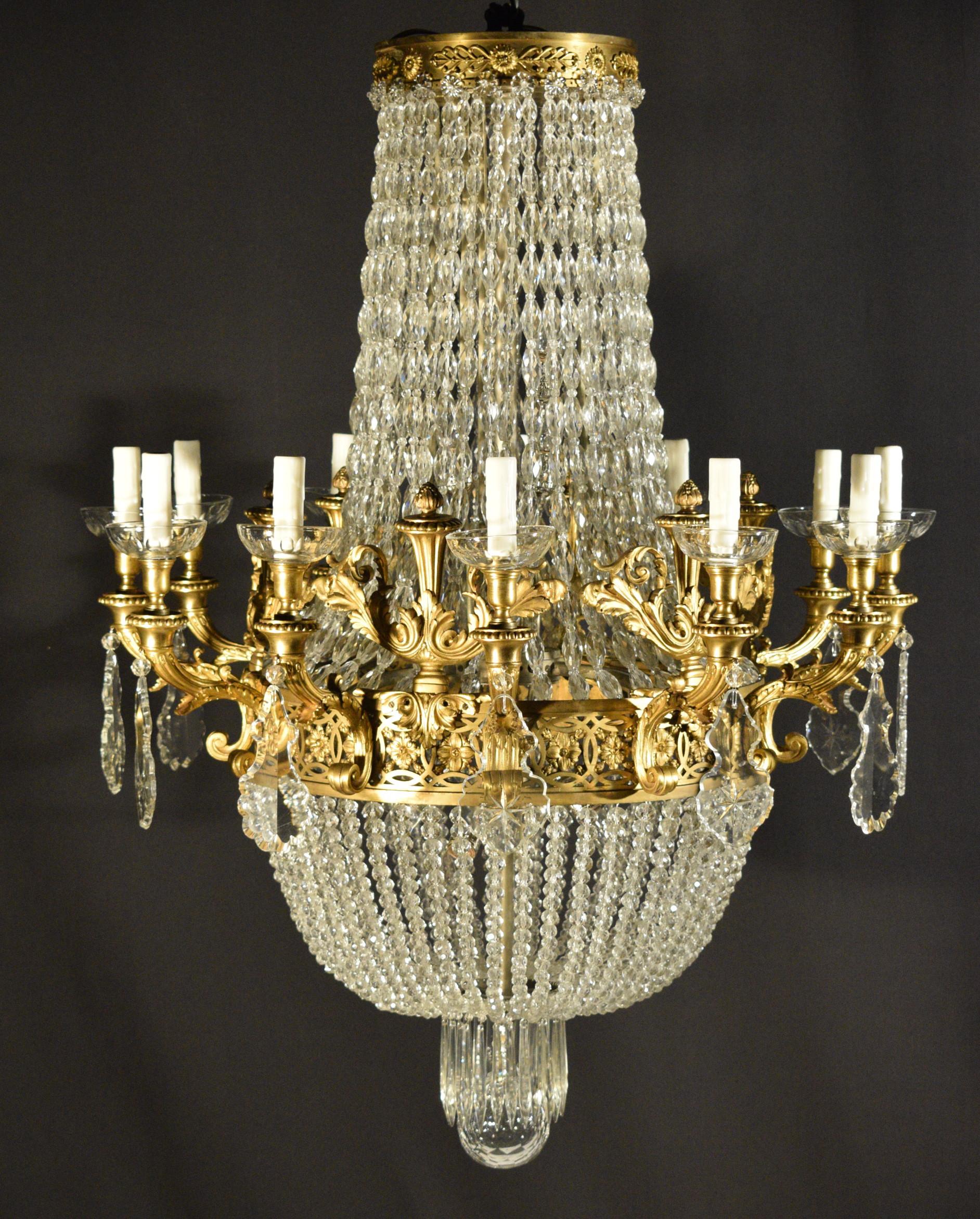 An exquisite gilt bronze and crystal chandelier. The pierced central circle issuing twelve scroll single arms and six ornamental finials. Delicate crystal chains delineating the classical basket shape. Crystal ball on the bottom. A truly magnificent