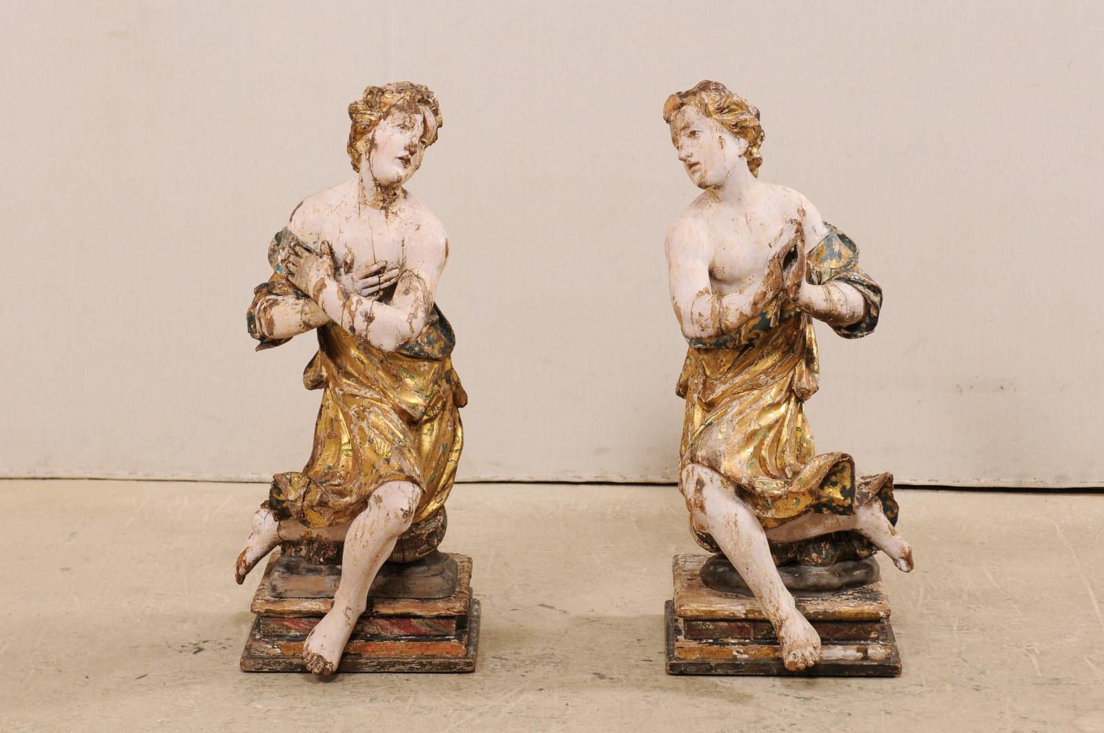 An exquisite Italian pair of carved and giltwood angelic male figures from the early 18th century. This pair of antique statues from Italy each feature a beautifully carved male figure, each draped within a gilt robe, with shoulders, arms, legs
