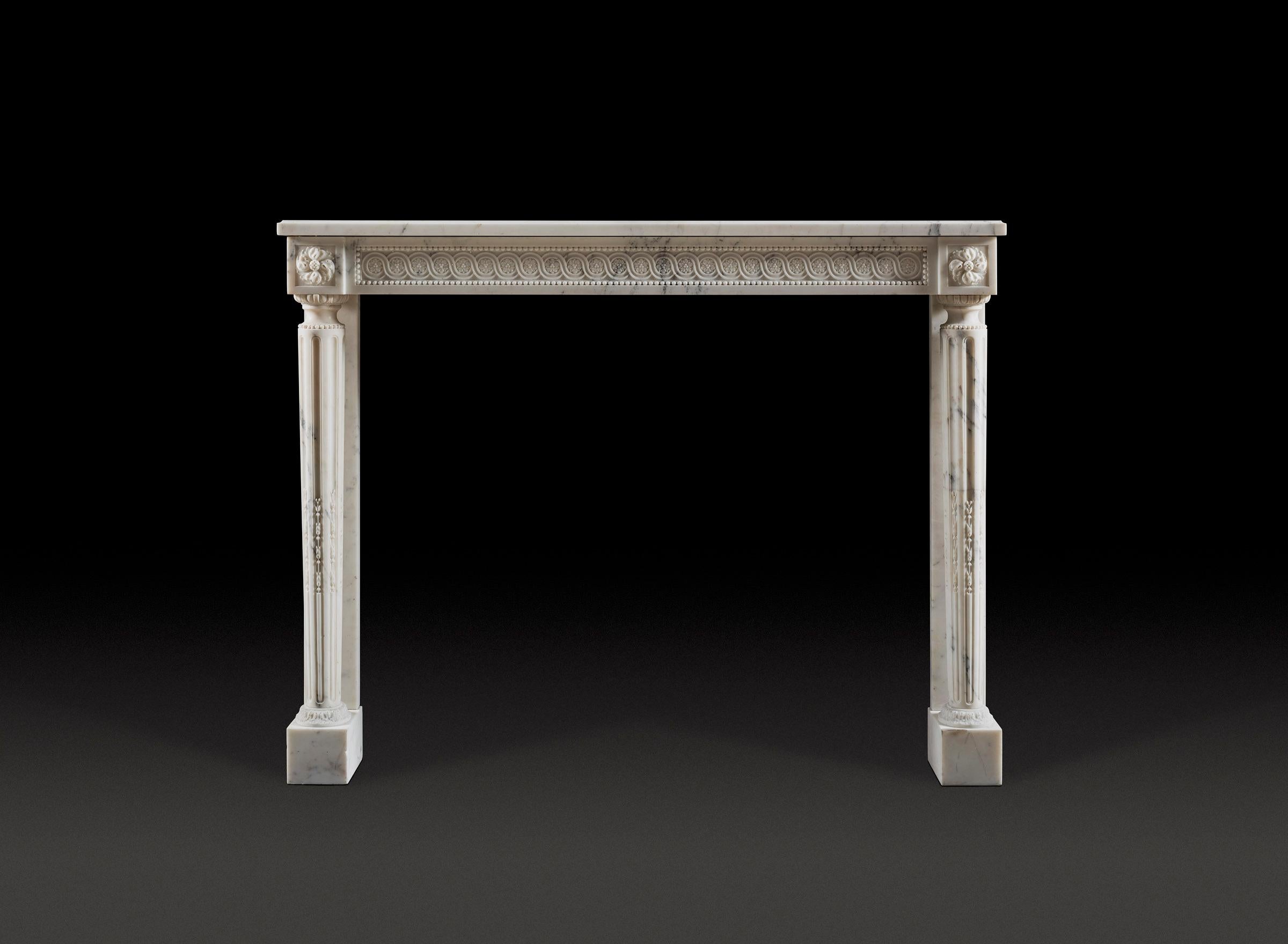 A very elegant Louis XVI style fireplace carved in Carrara marble, the running guilloche frieze flanked by paterae cornerblocks, supported by filled fluted column.

Height 43¾in (111cm) width 56½in (143.5cm)
Internal height 38¼in (97cm) width 46½in