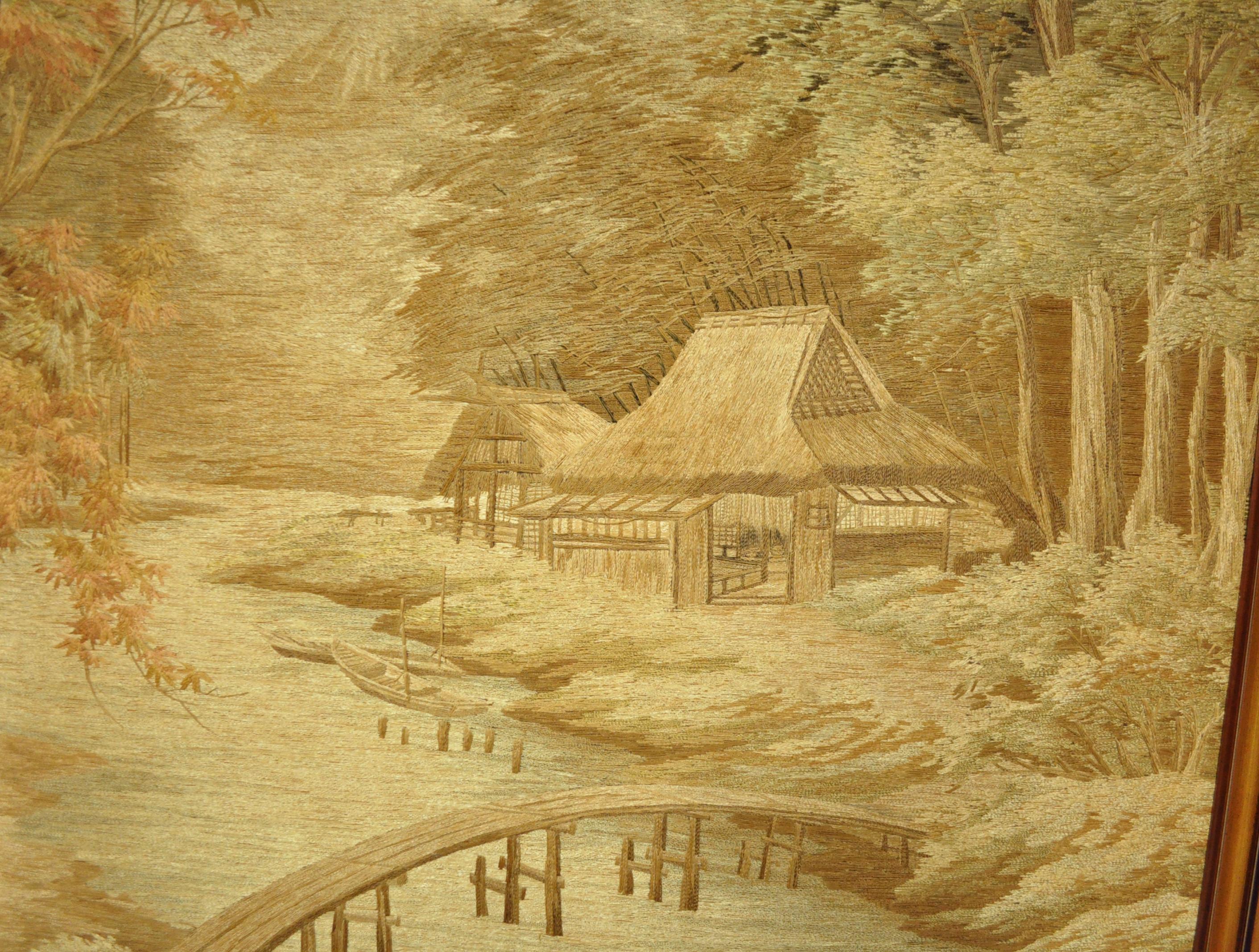 An extraordinary antique Japanese embroidered tapestry depicting an autumn forest scene with thatched cottage along a riverbank and Mt. Fuji in the far distance. The entire tapestry is created by hand embroidered individually laid satin stitch