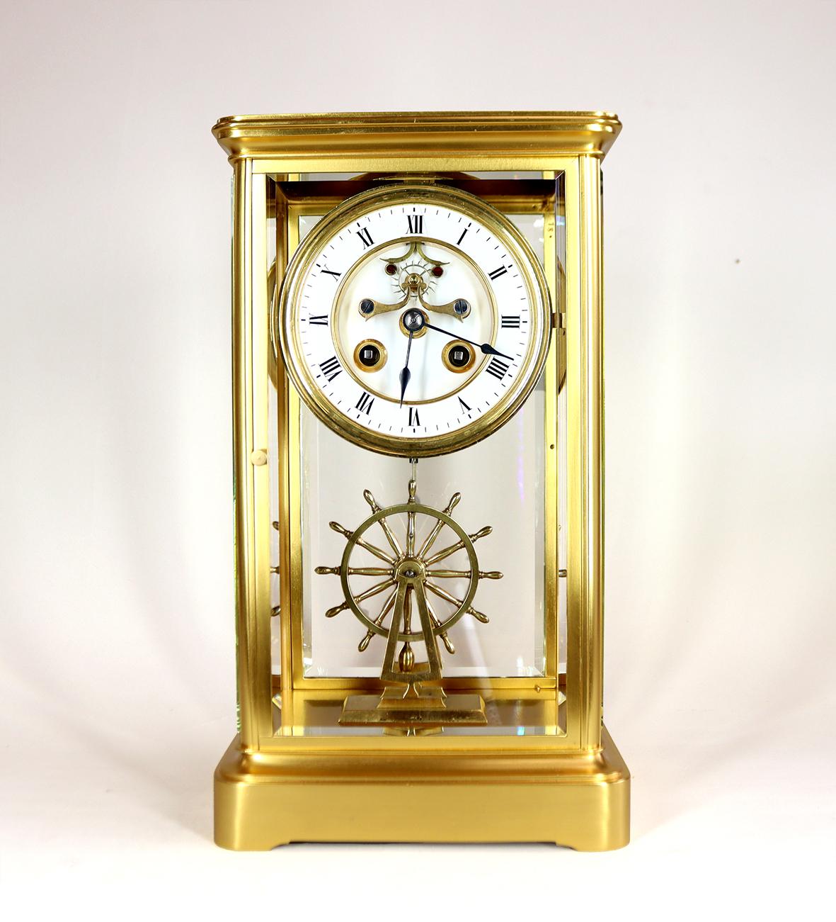 This Fine french four glass mantel clock has a beautifully gilded case with thick bevelled glass panels and doors. the eight day movement with visible jewelled Brocot escapement is mounted on a two part white enamel roman dial with blued spade