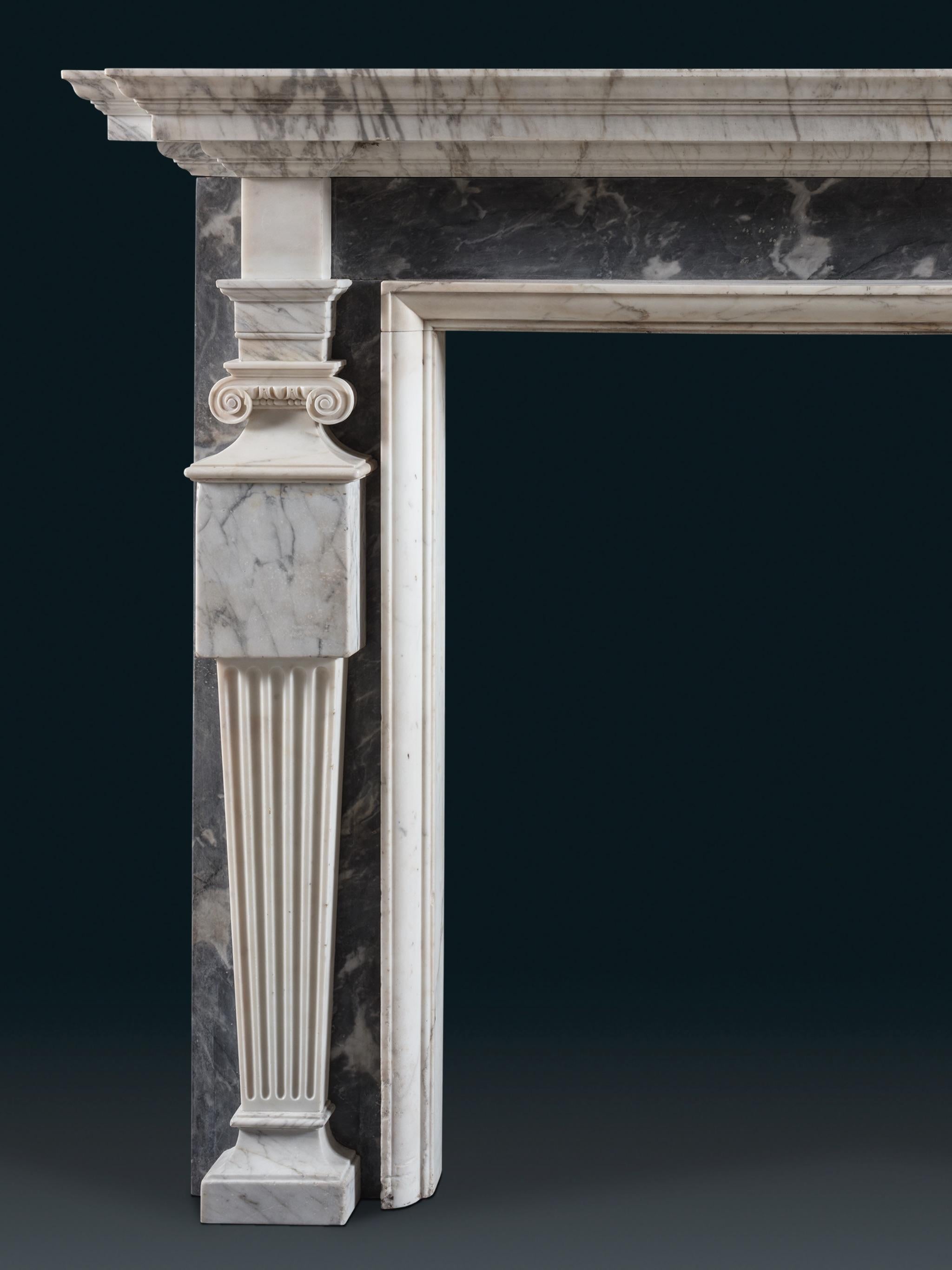 Un robusto camino del primo periodo georgiano nello stile di Inigo Jones. L'elegante ripiano sagomato in marmo Old English è sostenuto da una testata liscia in marmo Bardiglio. Gli stipiti hanno la forma di colonne affusolate sormontate da capitelli