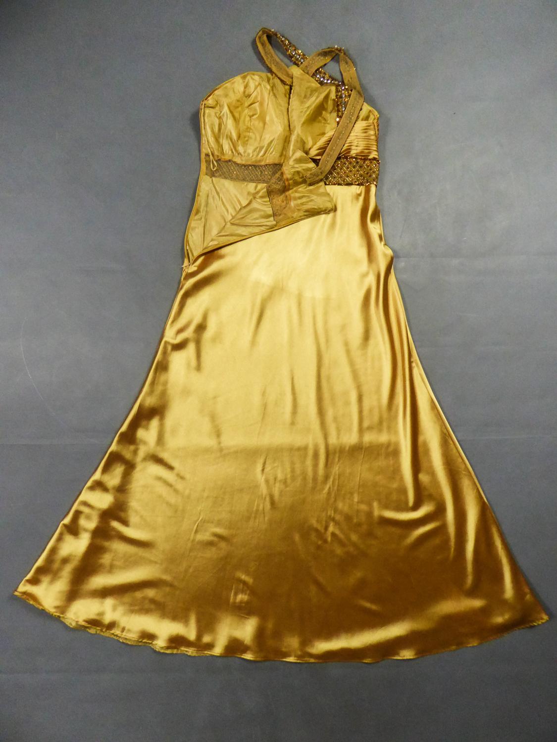 Circa 1980
France

Elegant Music-Hall evening dress in gold Duchess satin embroidered with sequins from the 1980s. Large backless cleavage with crossed straps and embroidered with sequins and rhinestones on cream tulle. High-waisted bustier with