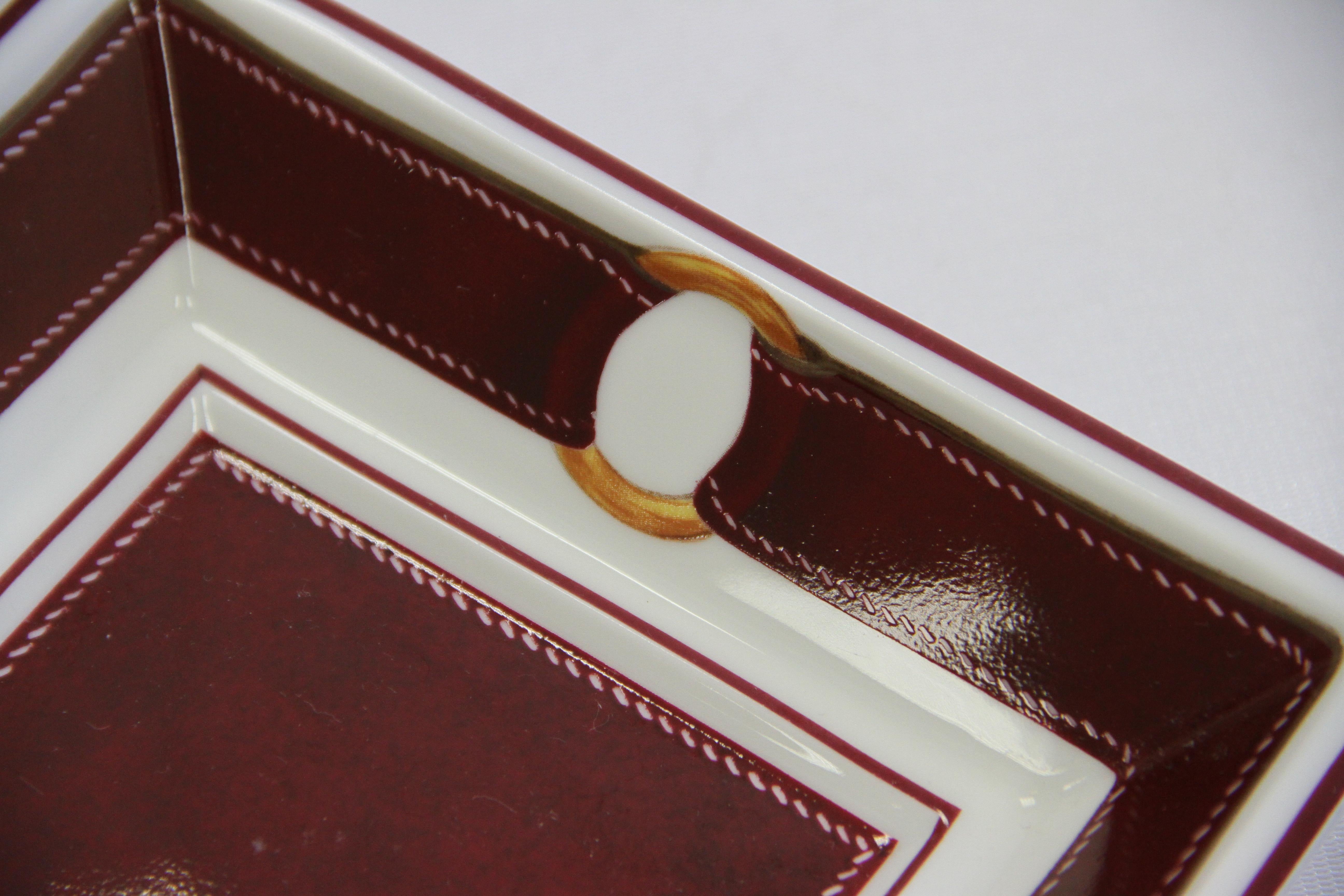 Of square shape. In fine porcelain de Limosges (Fine Porcelaine de Limoges), decorated with a dark red leather bows.
Red Suede to the underside. Stamped with the 