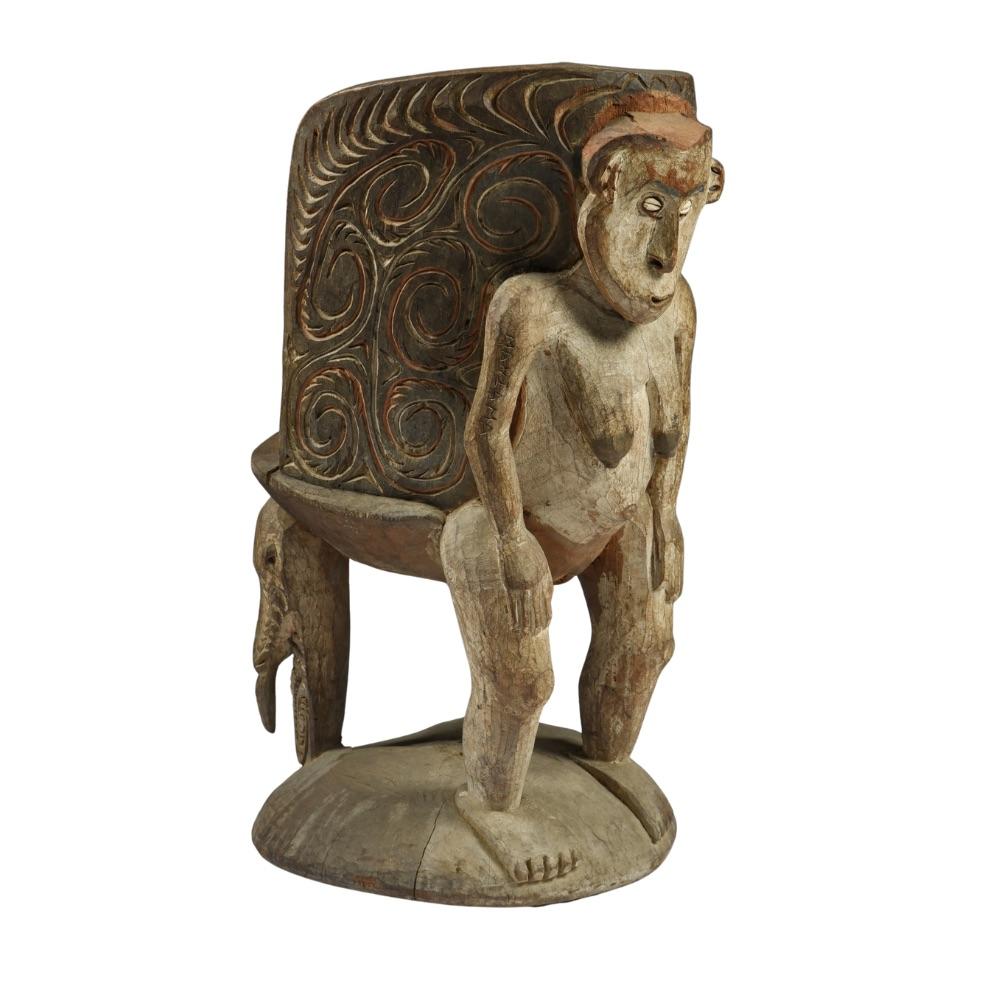 An Iatmul Orator’s Stool – Papua New Guinea. First half 20th Century

The curved back with carved stylised decoration and with a standing female figure with inset cowrie shell eyes and previously with resin/mud to the top of the head, her right arm