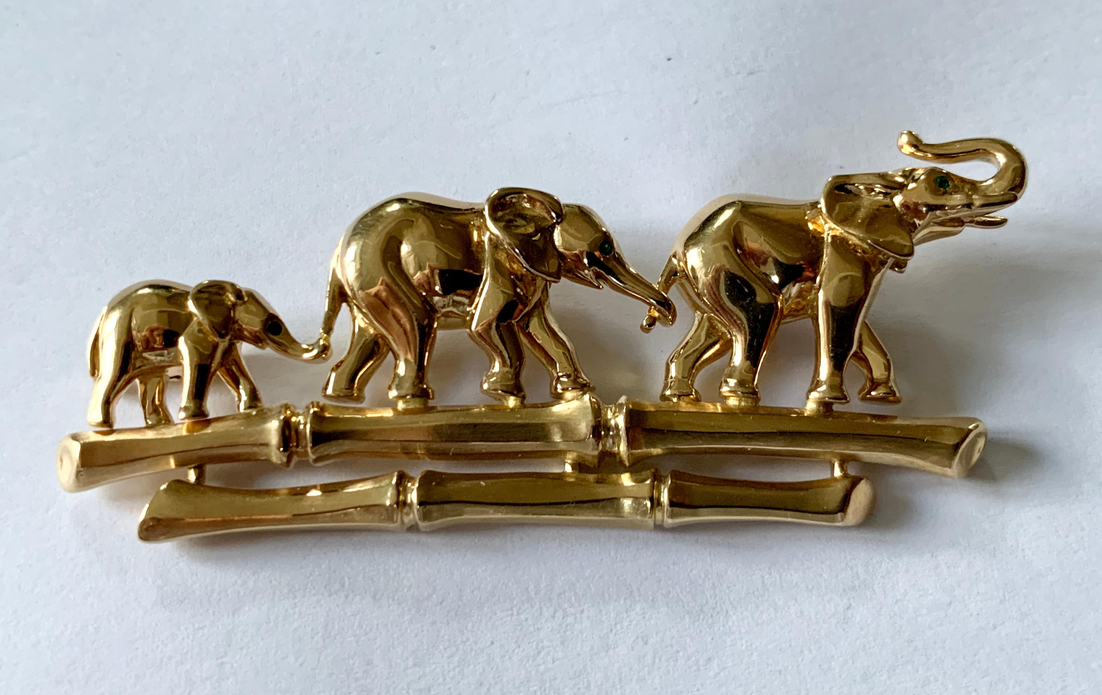 Broche vers 1980, représentant une famille d'éléphants marchant le long d'un sentier de bambous, en or jaune 18 K, polie et brossée, tous les éléphants ayant un œil en émeraude taillée en cercle, signée Cartier, numérotée.  651049, marque de
