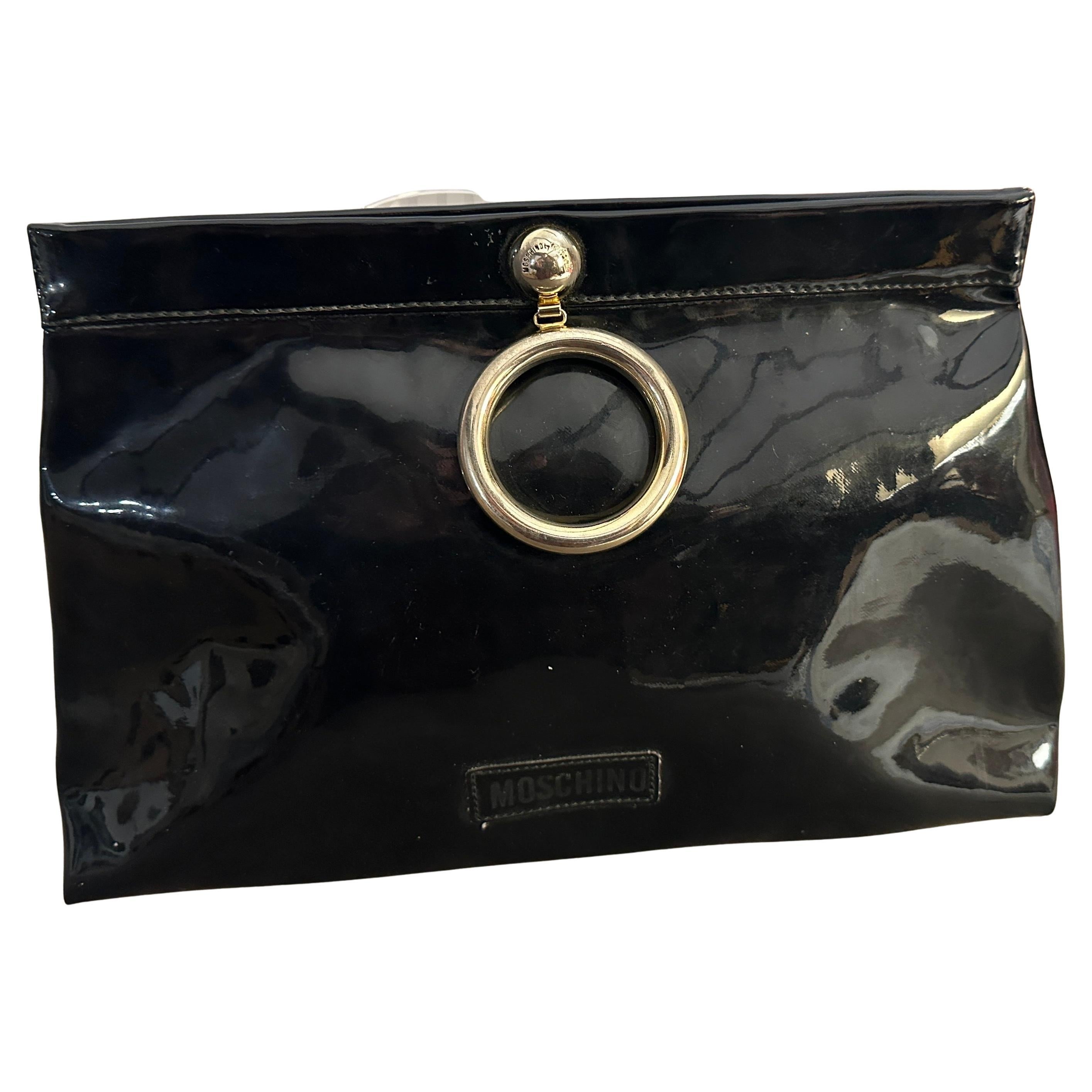 This iconic 1980s Franco Moschino handbag is a bold and playful statement piece, embodying the designer's signature avant-garde style. Crafted from glossy blue plastic, the bag features a sleek, structured silhouette with a high-shine finish that