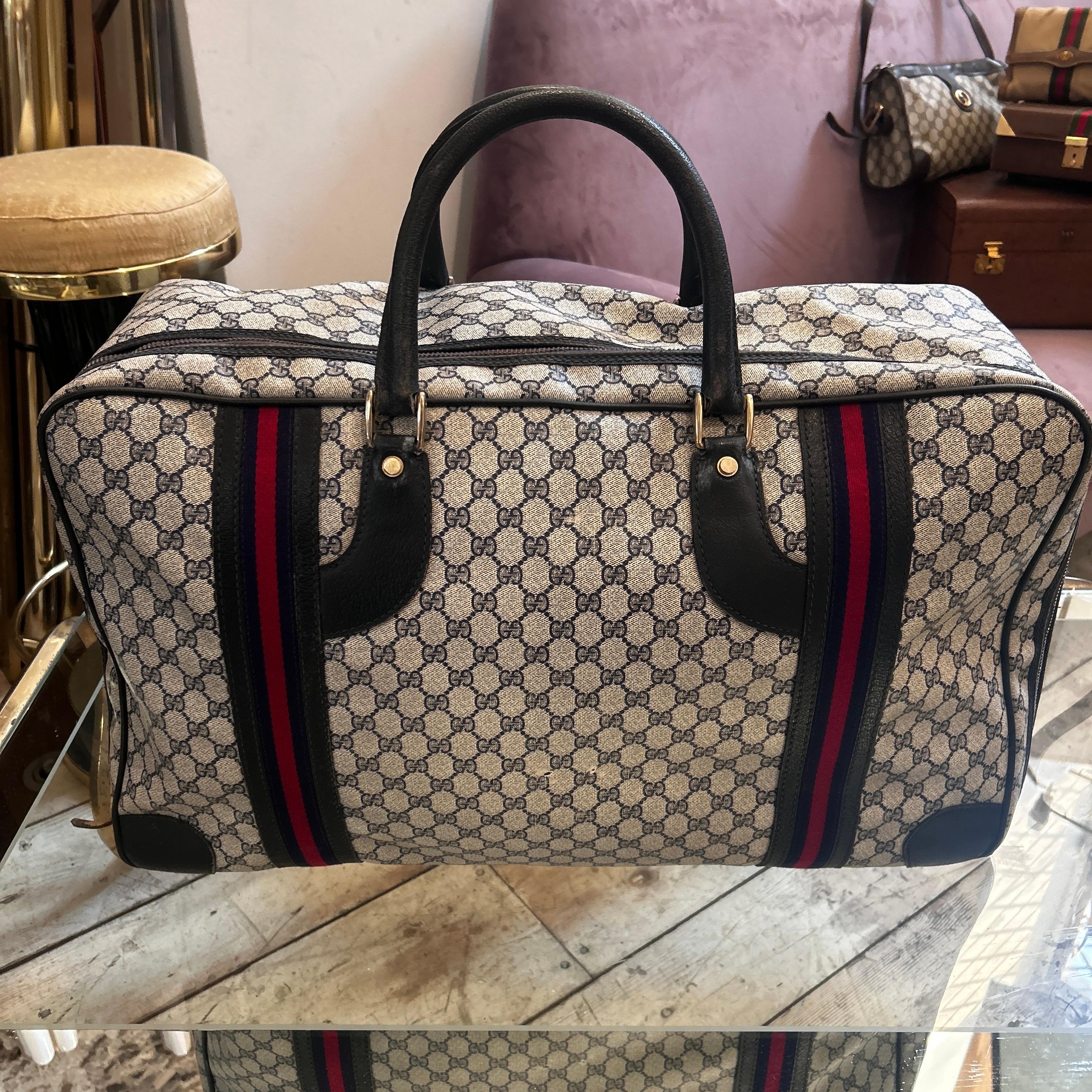 This vintage Gucci travel bag from the 1980s embodies the brand’s timeless elegance and attention to detail. Crafted from Gucci’s signature GG monogram canvas in beige and brown, it features two vertical web stripes in deep red and navy blue, adding