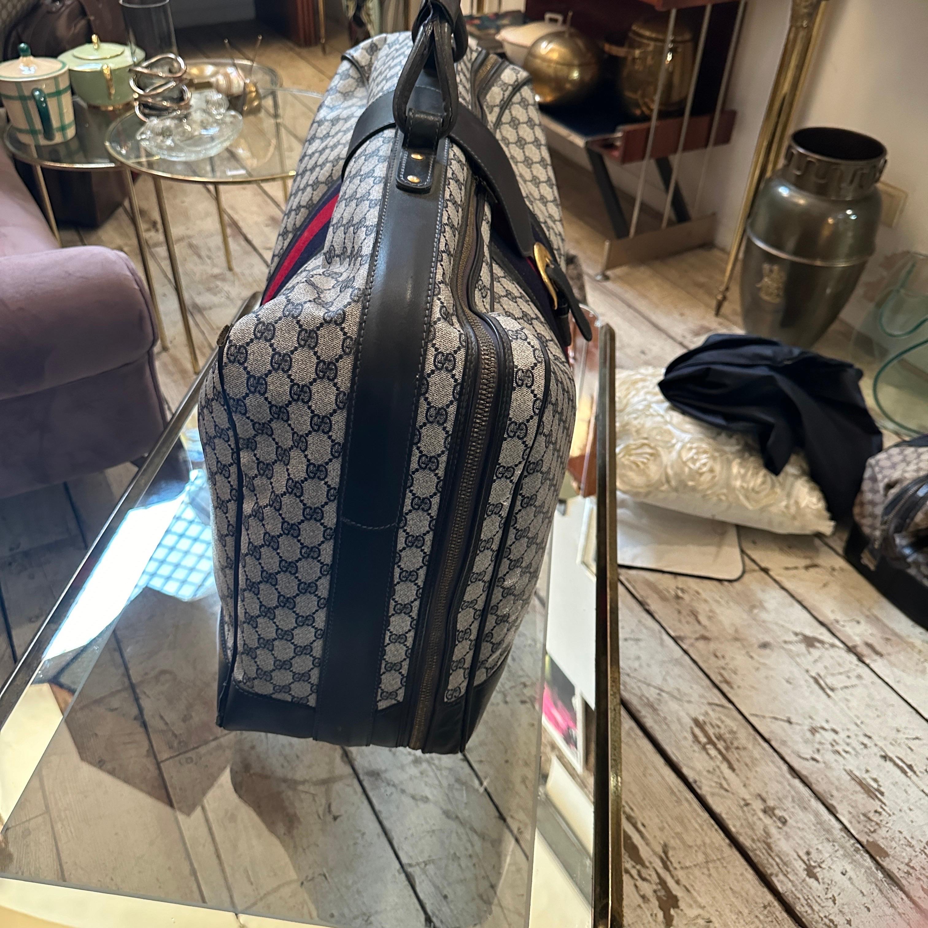 This vintage Gucci travel bag from the 1980s embodies the brand’s timeless elegance and attention to detail. Crafted from Gucci’s signature GG monogram canvas in beige and brown, it features a vertical web stripe in deep red and navy blue, adding