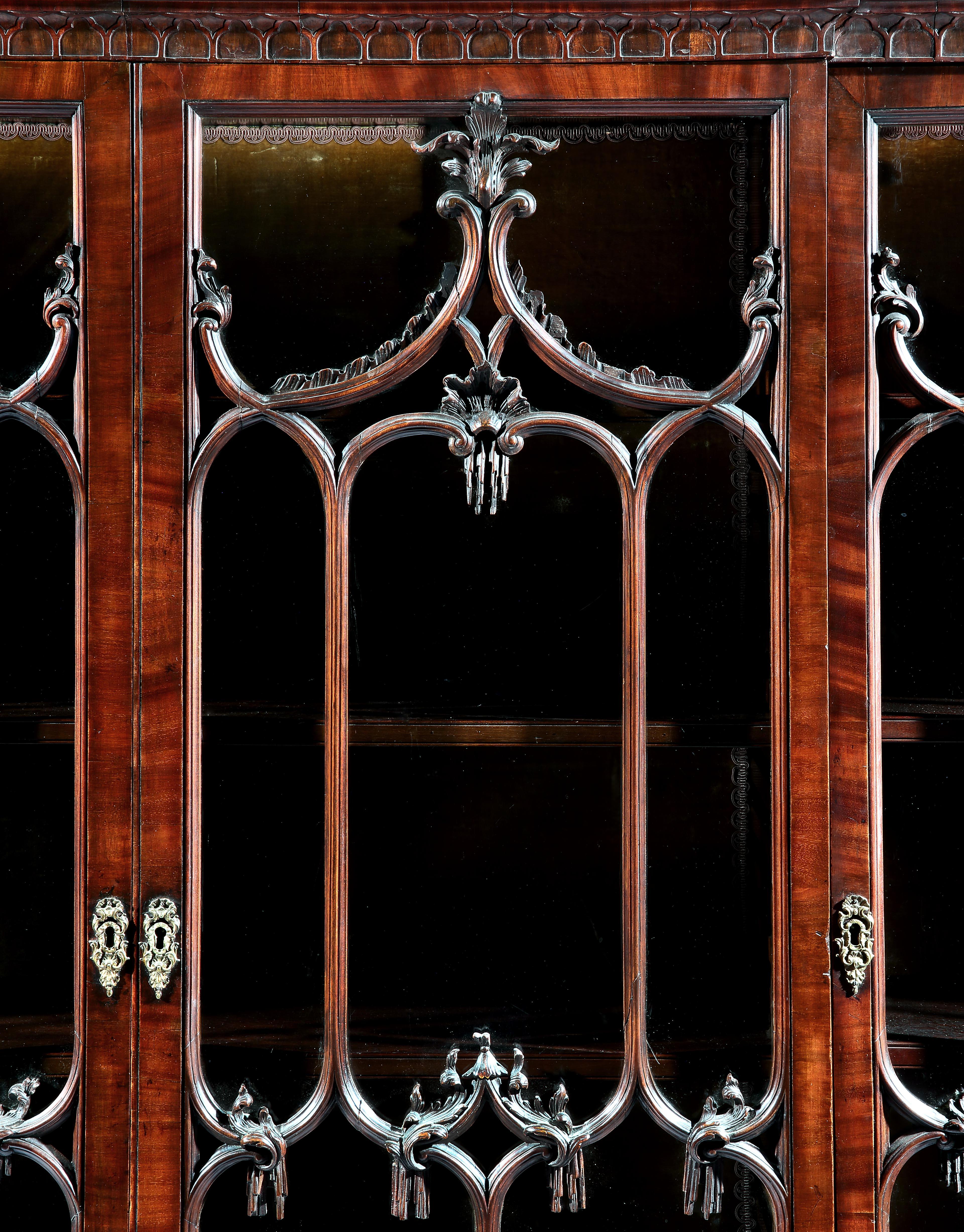 An Important George II Chippendale Period mahogany breakfront bookcase.
The open fretwork swan neck cornice with a Gothic blind fretwork cushion moulding, above four glazed doors carved with central shells below flowing acanthus, resting on a four