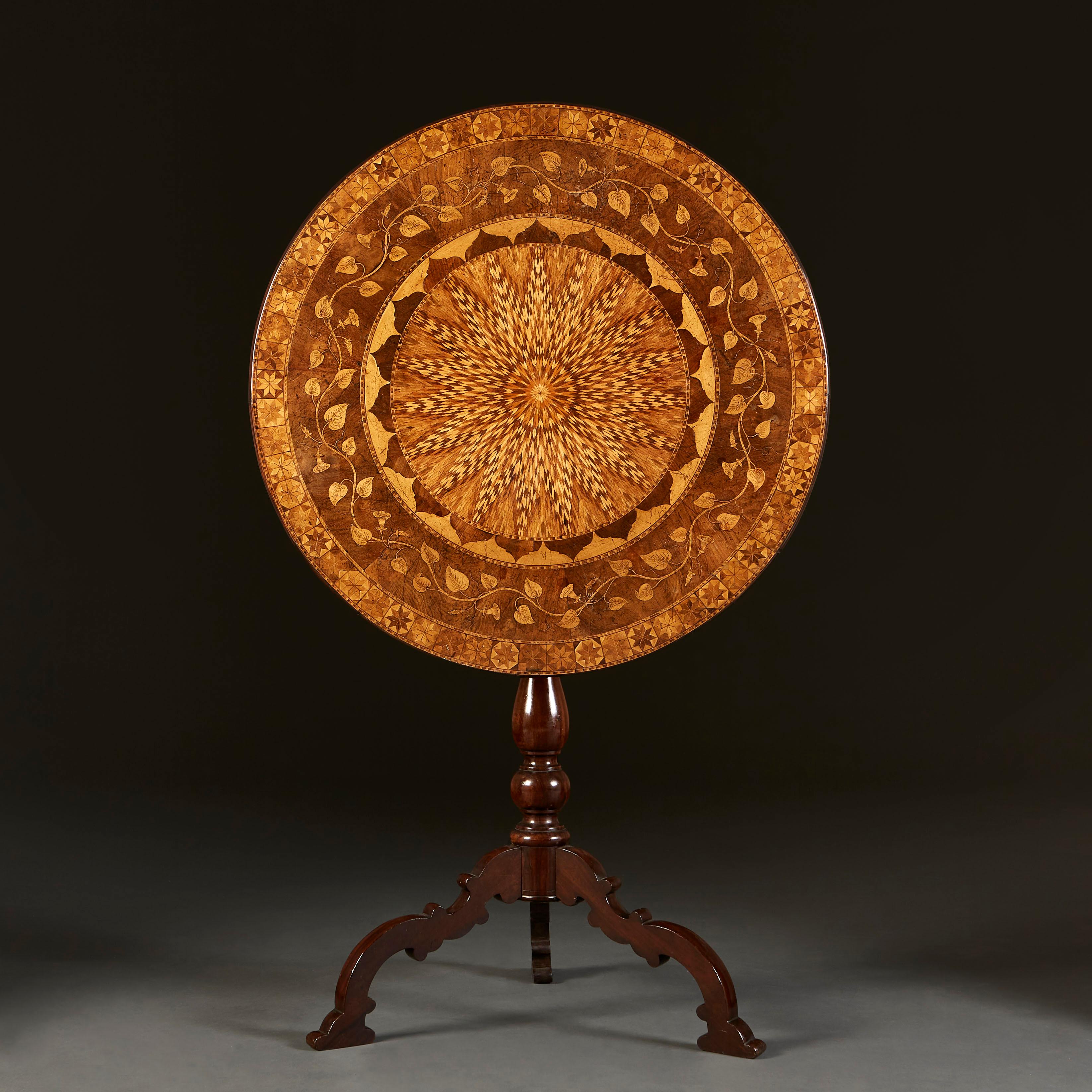 An early nineteenth century marquetry table, with a variety of exotic woods inlaid to create a central medallion design, circled by an intertwining vine border, in turn bordered by a variegated star motif. The table top tilts to reveal a hidden