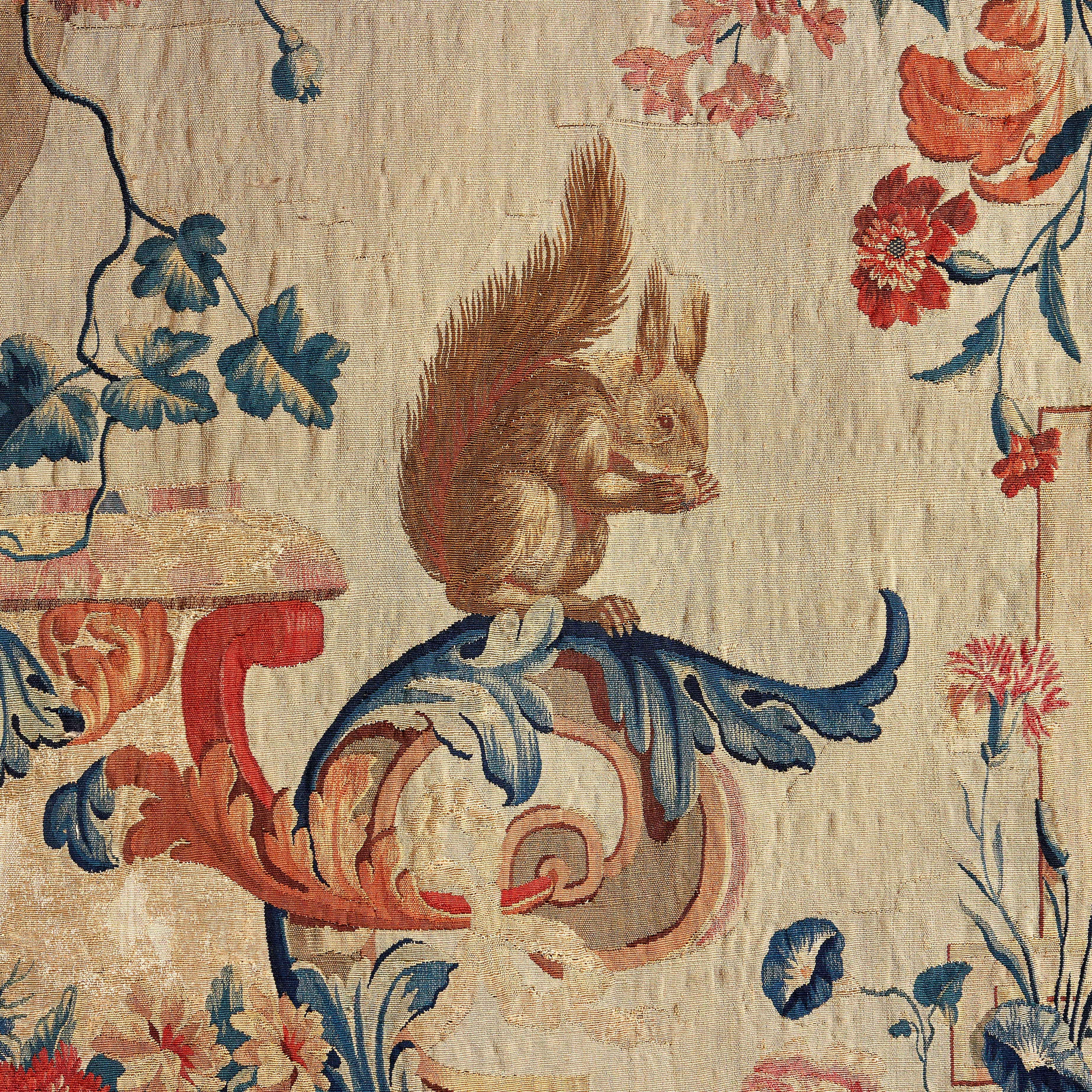 A rare mid eighteenth century Rococo tapestry, the central field decorated with a vase and cornucopia of flowers, resting on a marble plinth with scallop shell below and eagle with out swept wings. To the right of the vase, a perched squirrel, the