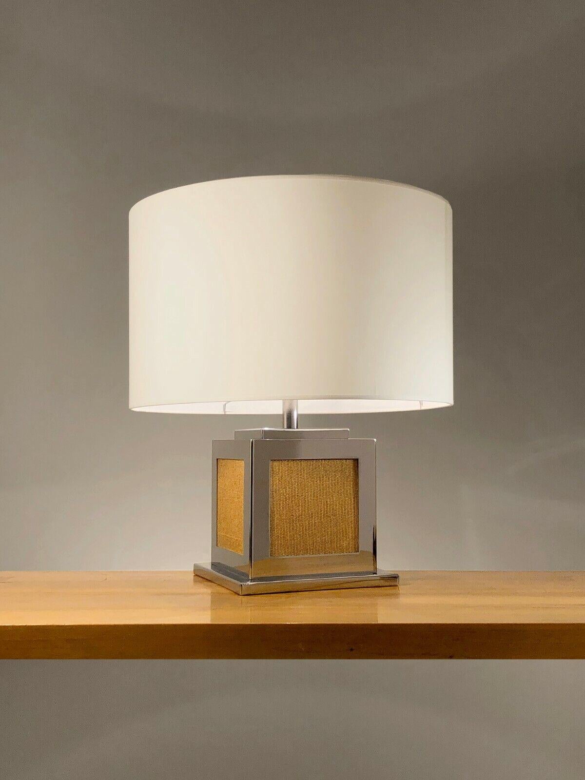 A generous and rigorous cubic table lamp, Post-Modernist, Shabby-Chic, stepped base in chrome metal with a square section enhanced by beige fabric tops, topped with a large cylindrical lampshade, to be attributed, France 1970- 1980.

DIMENSIONS: H