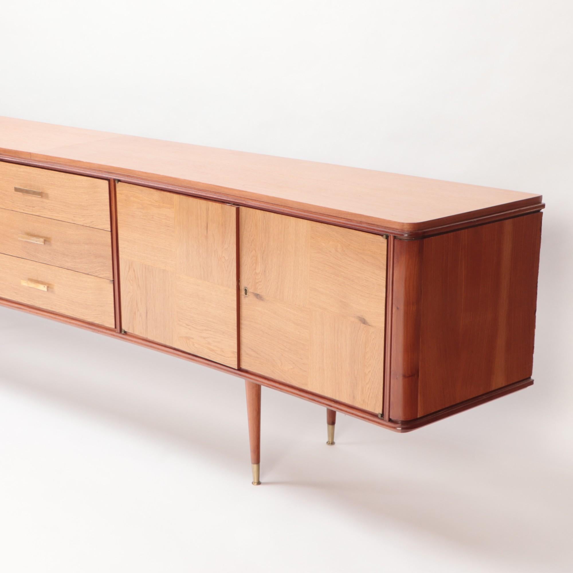 An imposing Mid-Century Modern sideboard having three central drawers flanked by a pair of doors and raised on round tapering legs ending in brass sabots.